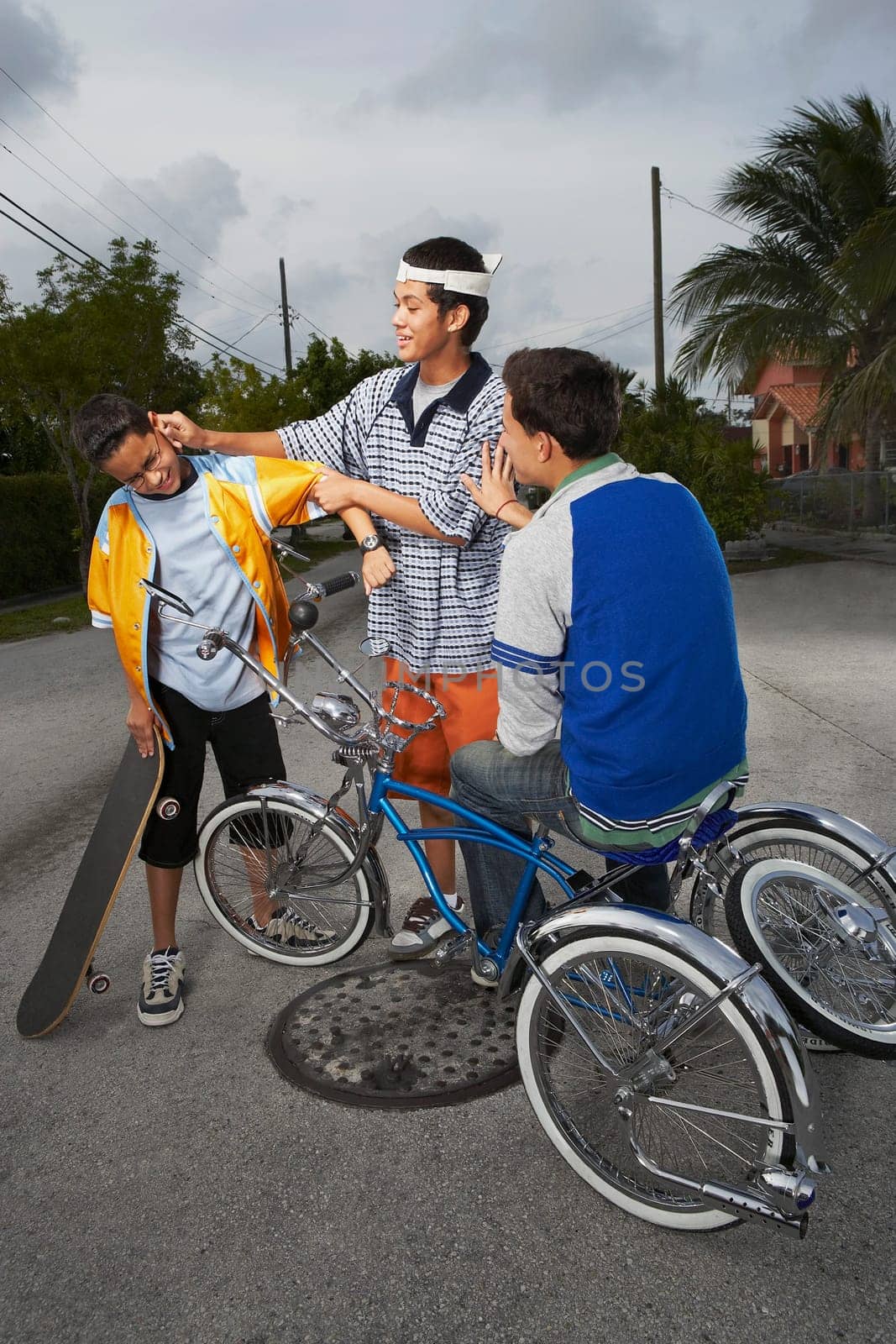 Teenage boy sitting on a low rider bicycle and looking at his friend pulling the ear of a boy