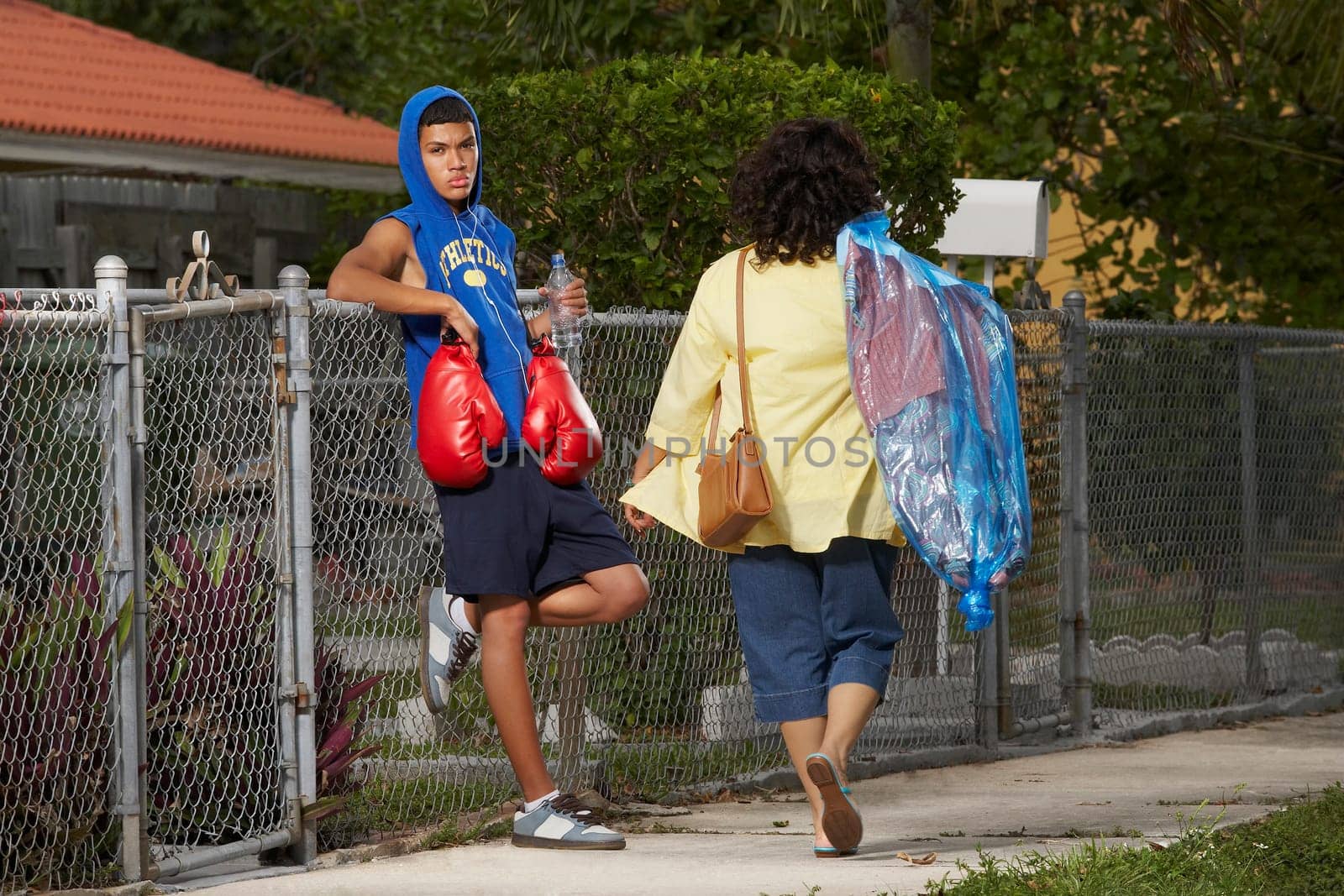 Rear view of a mature woman walking with a teenage boy leaning on a chain-link fence