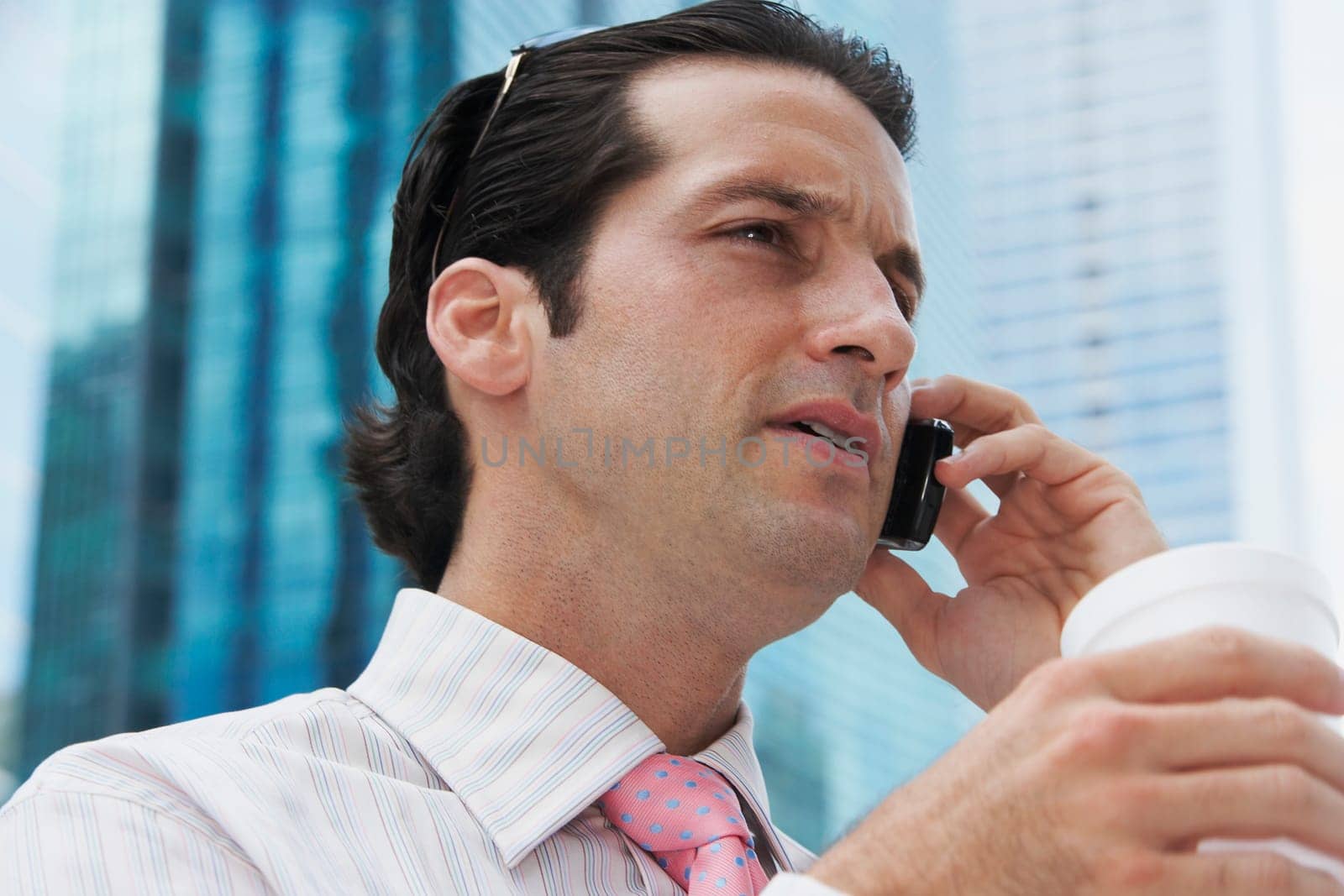 Close-up of a businessman holding a disposable cup and talking on a mobile phone