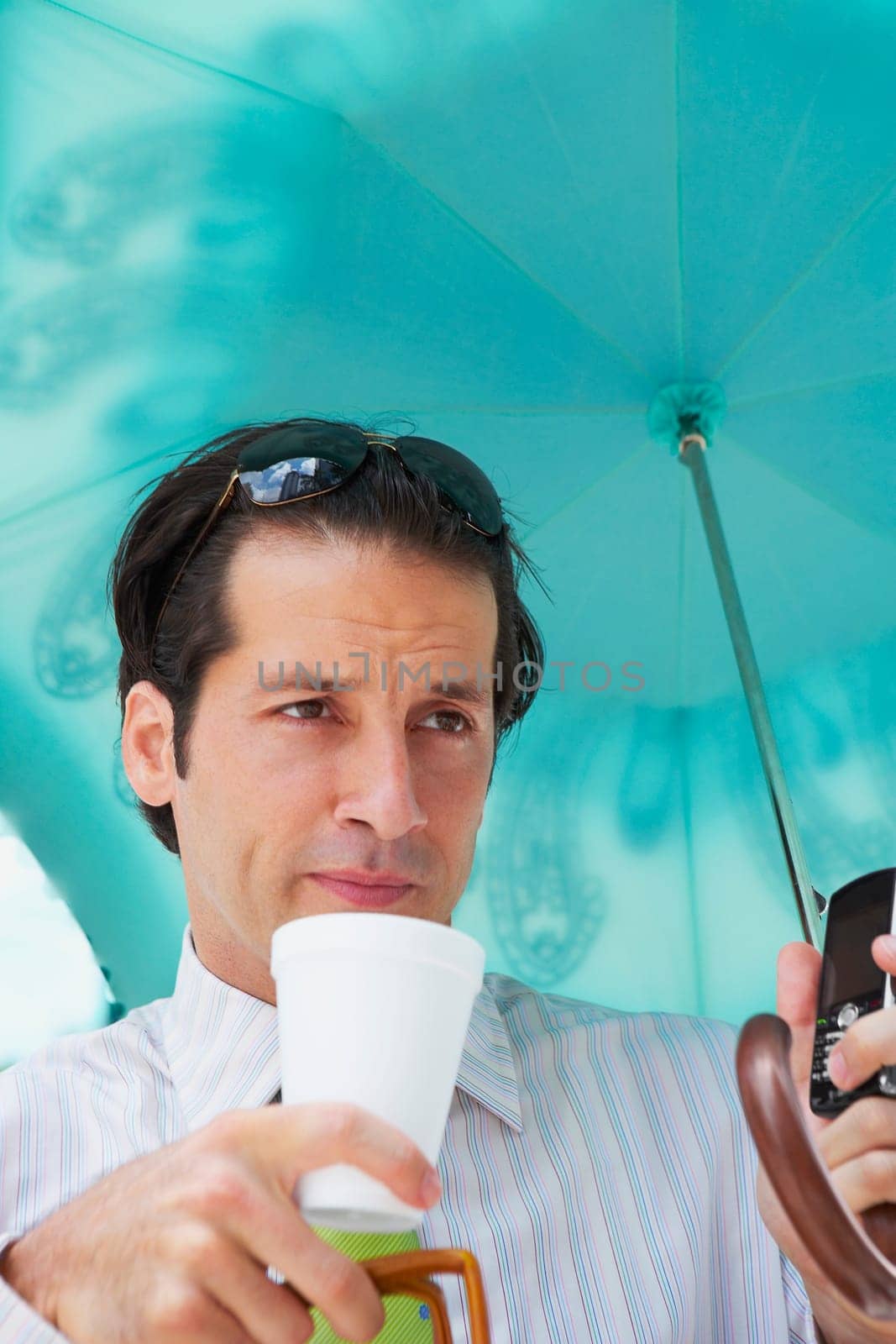 Close-up of a businessman holding an umbrella and drinking cold drink