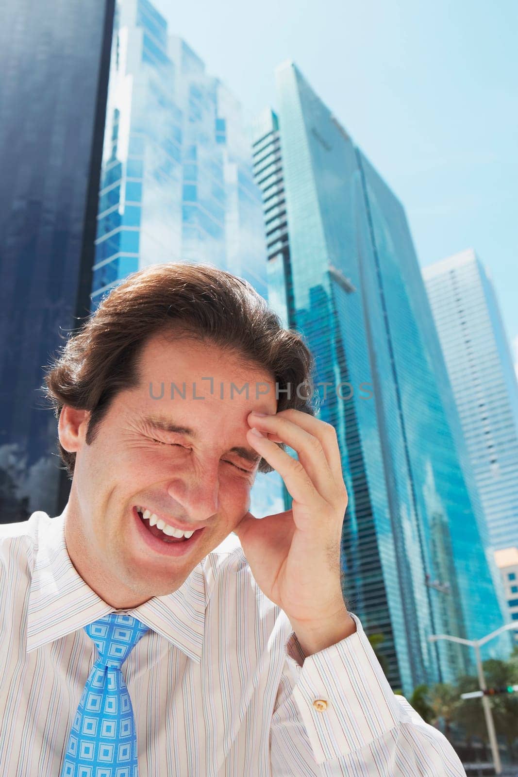 Businessman laughing with his head in his hand in front of office buildings