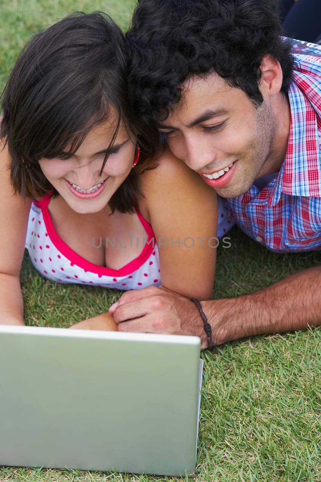 Close-up of a young couple lying in a lawn in front of a laptop