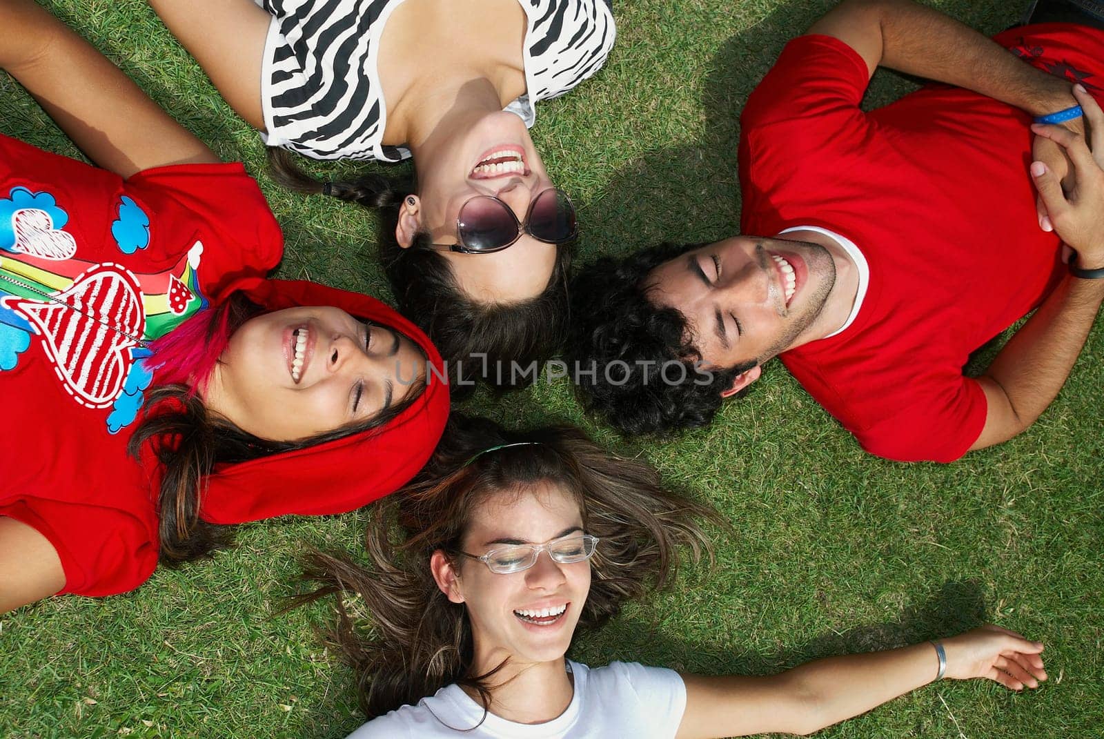 Three young women with a young man lying on grass and smiling