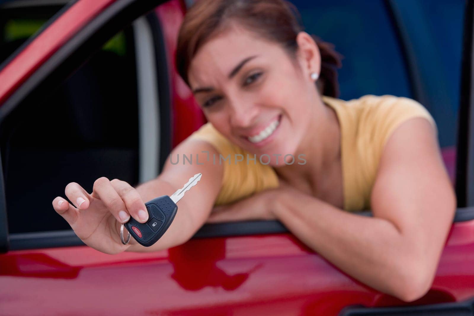 Portrait of a young woman leaning on the window of a car and showing a car key