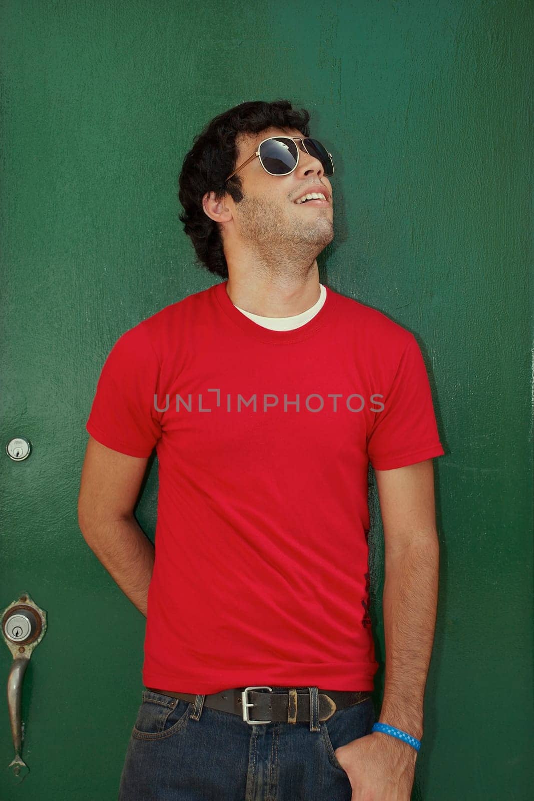 Young man standing in front of a closed door and wearing sunglasses