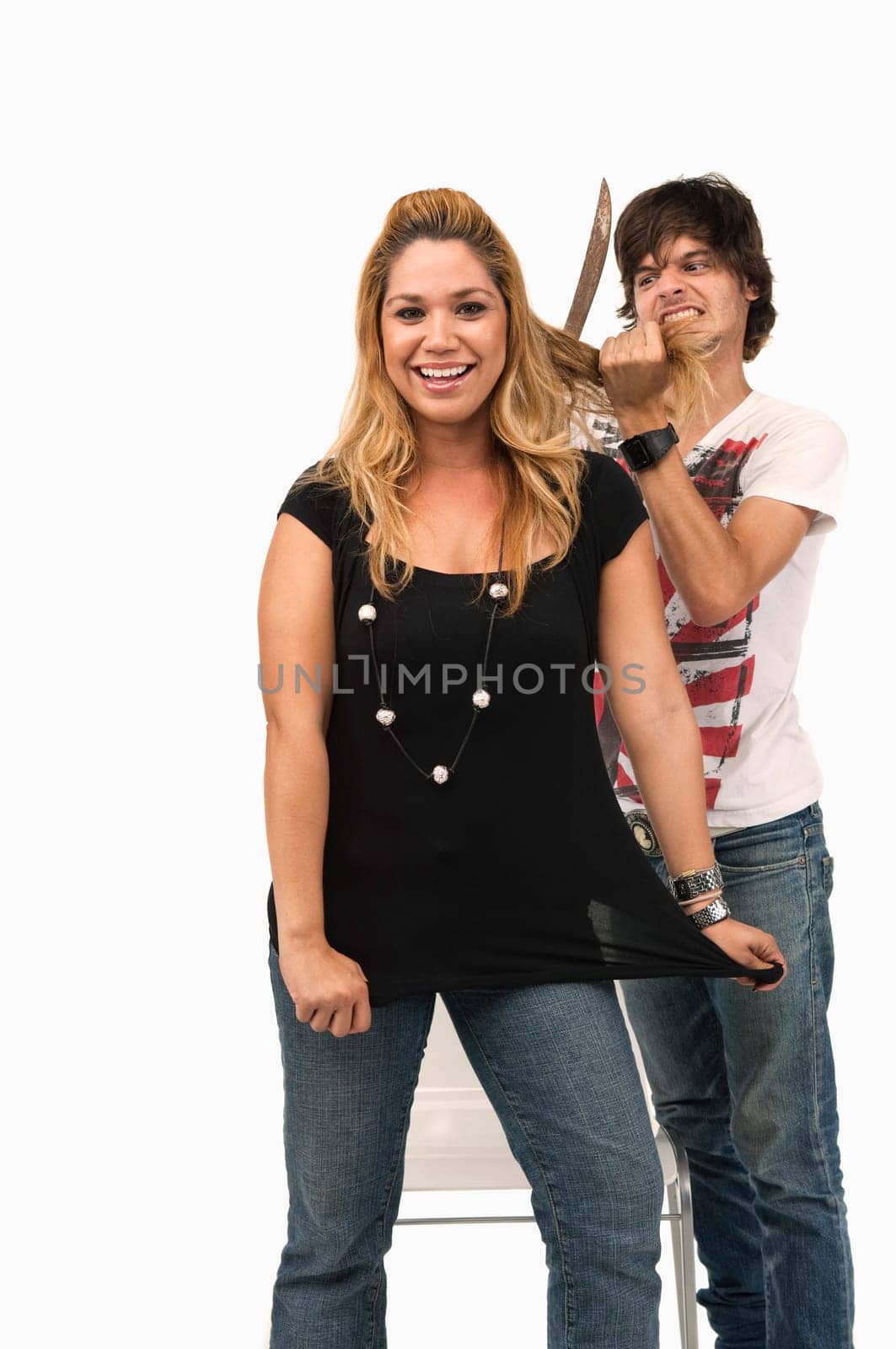 Portrait of a young woman smiling with a young man cutting her hair with a knife behind her