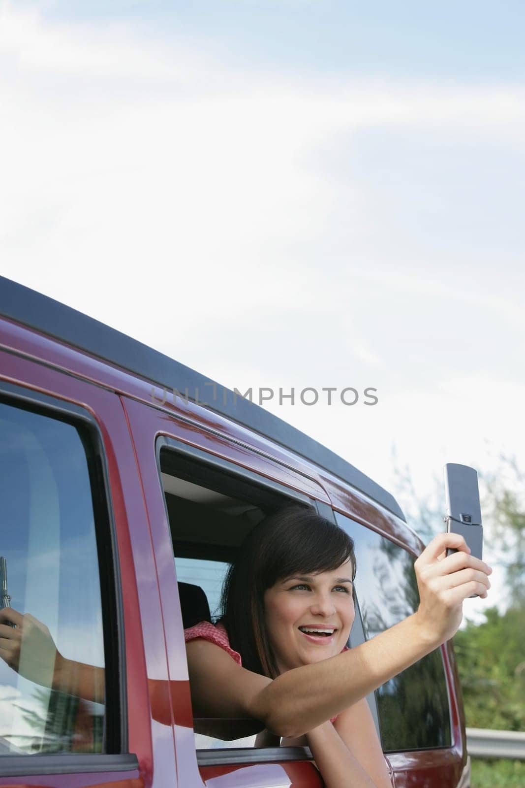 Young woman sitting in a car and taking a picture with a mobile phone