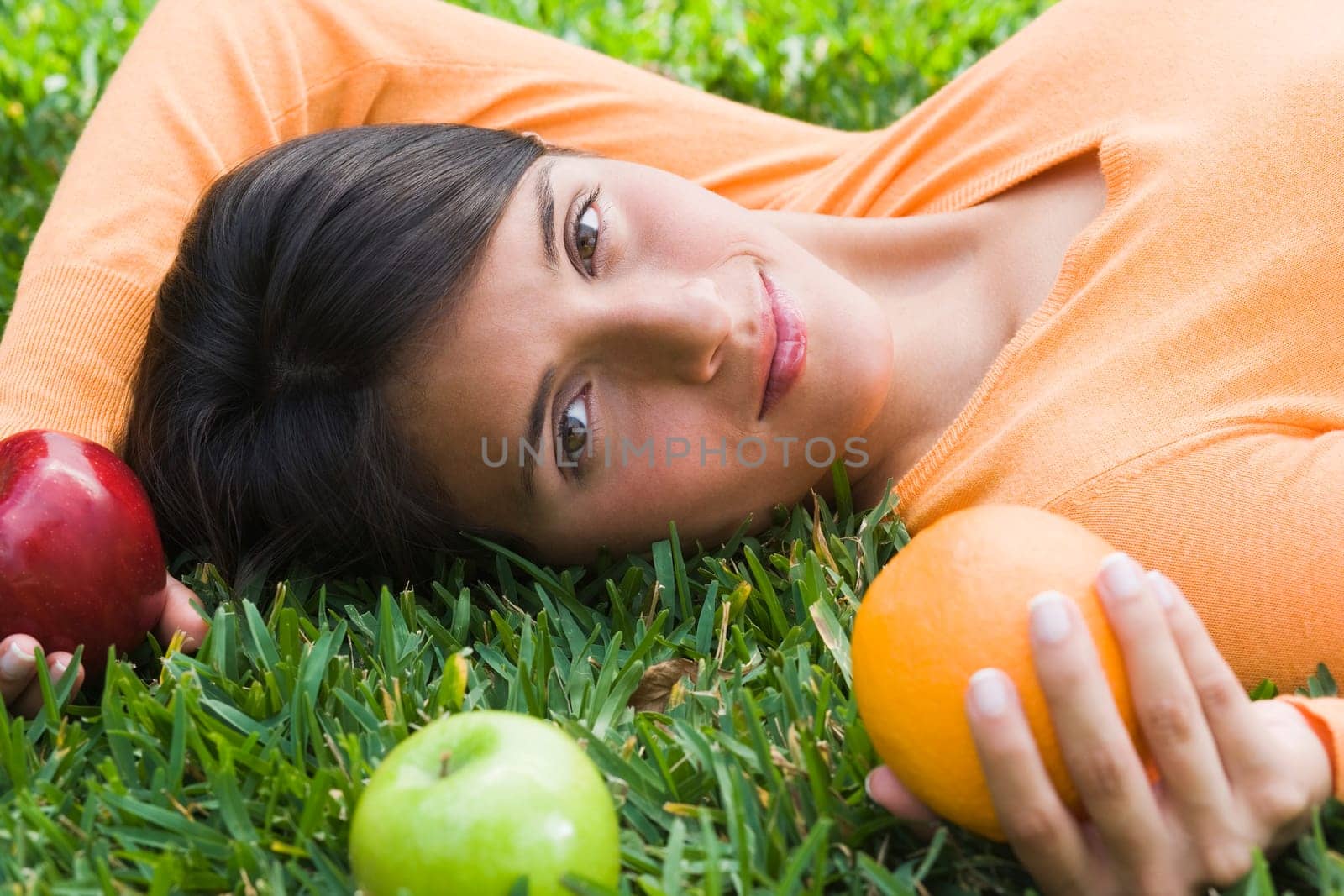 Teenage girl lying on grass and holding fruits
