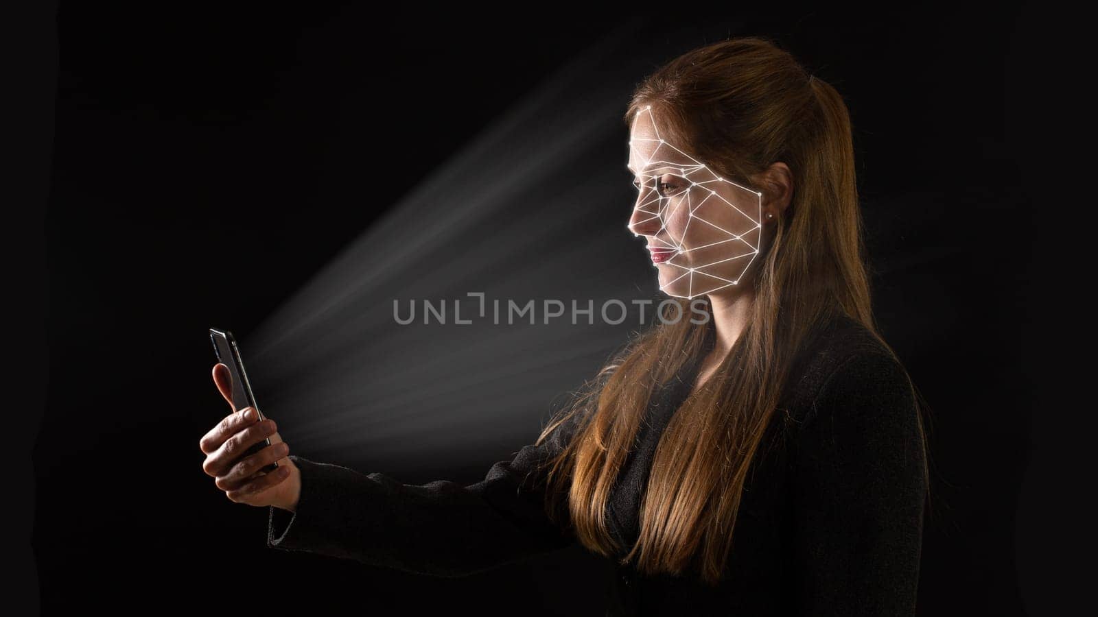 Young Caucasian businesswoman using biometric technology in her phone with light glowing on her. Concept of face recognition and identification to authorize access. Adult on dark background.