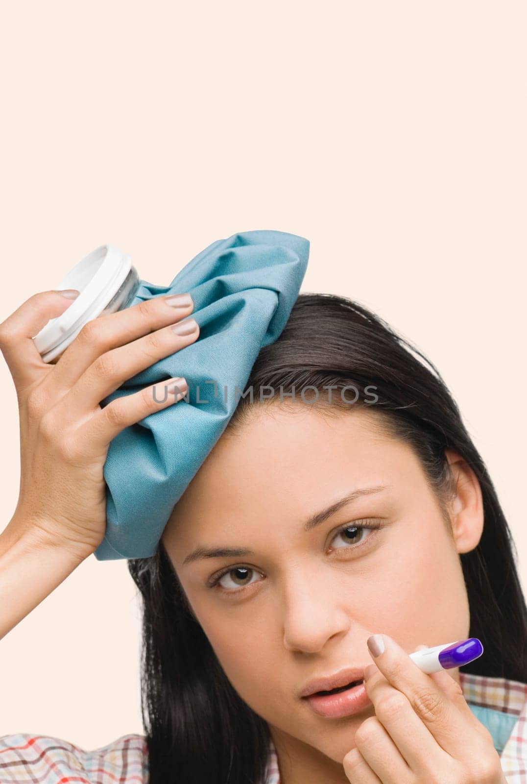 Portrait of a young woman measuring her temperature with a thermometer and holding an ice pack on her head