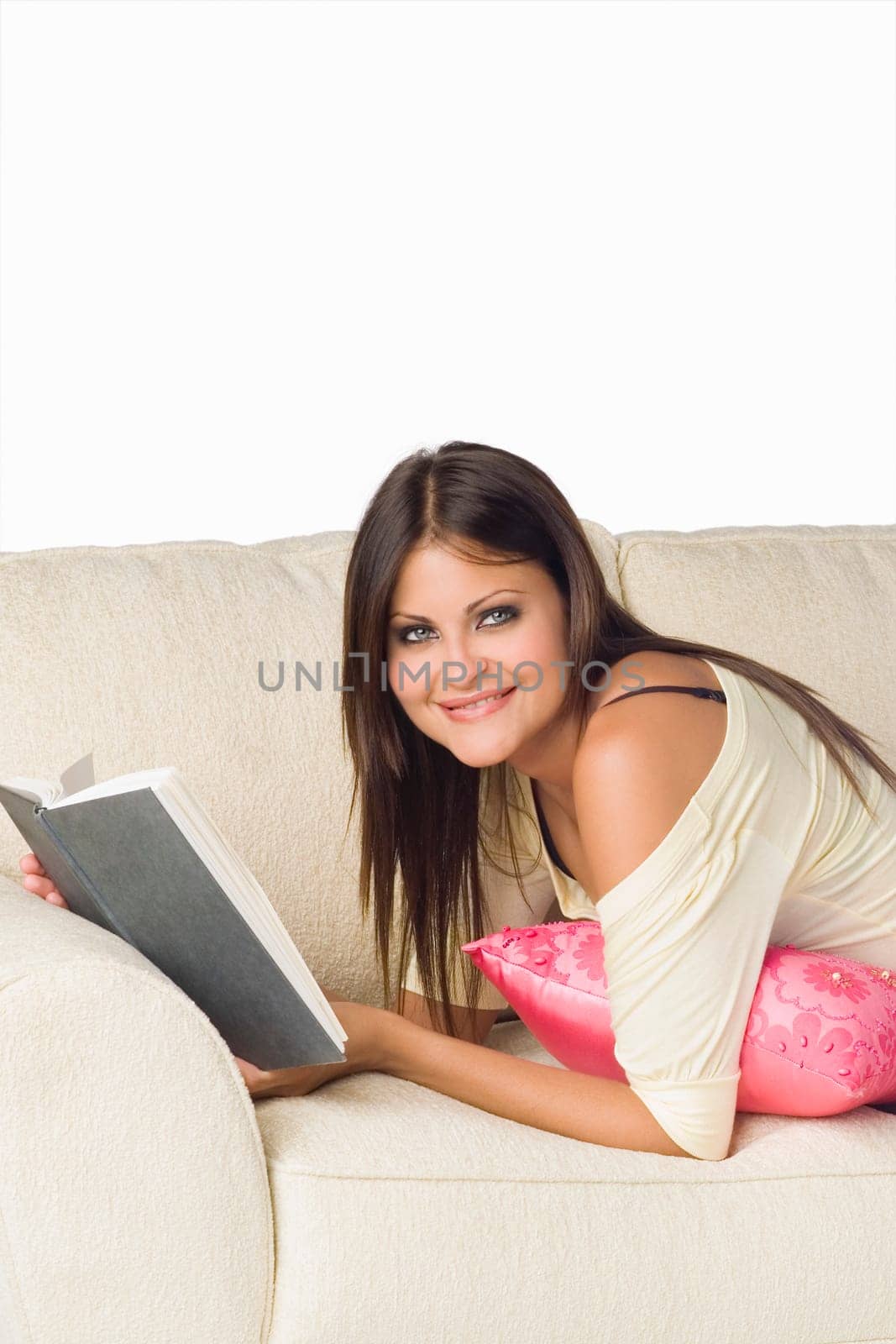 Portrait of a young woman lying on a couch and holding a book