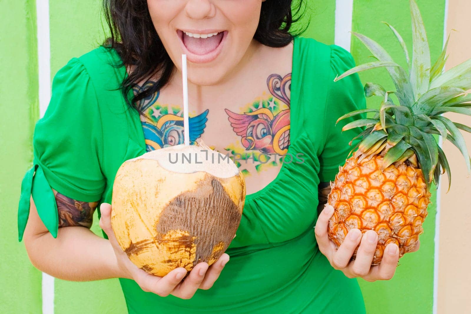 Mid section view of a young woman holding a pineapple and drinking coconut milk with a drinking straw