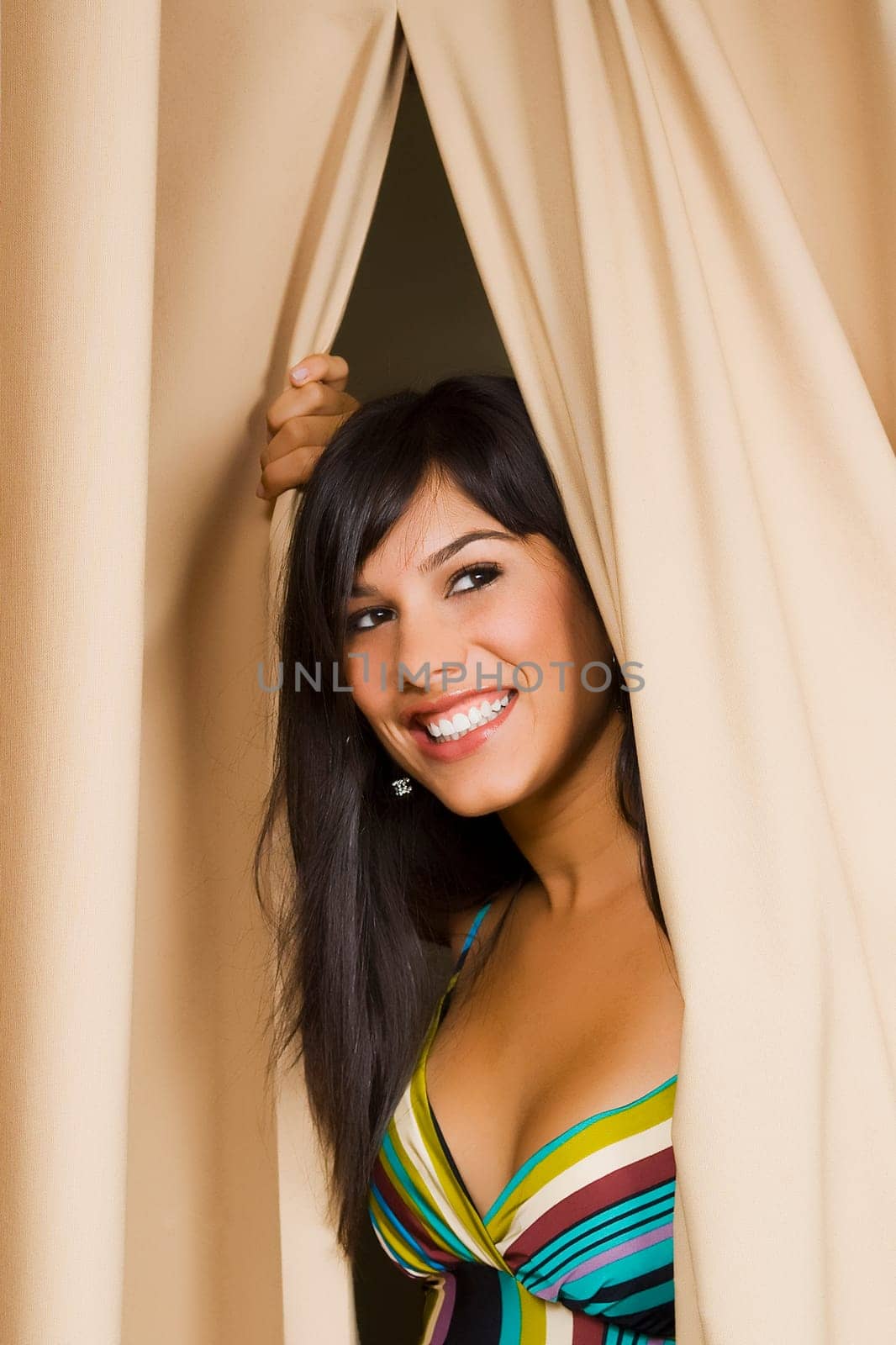 Young woman peeking through a curtain and smiling