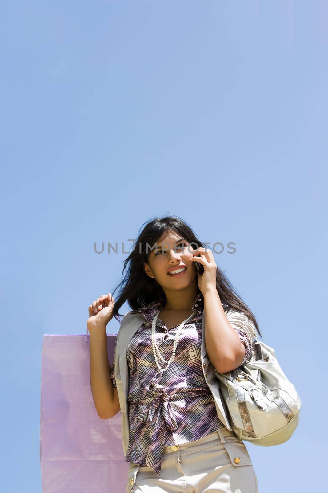 Low angle view of a young woman holding shopping bags and talking on a mobile phone