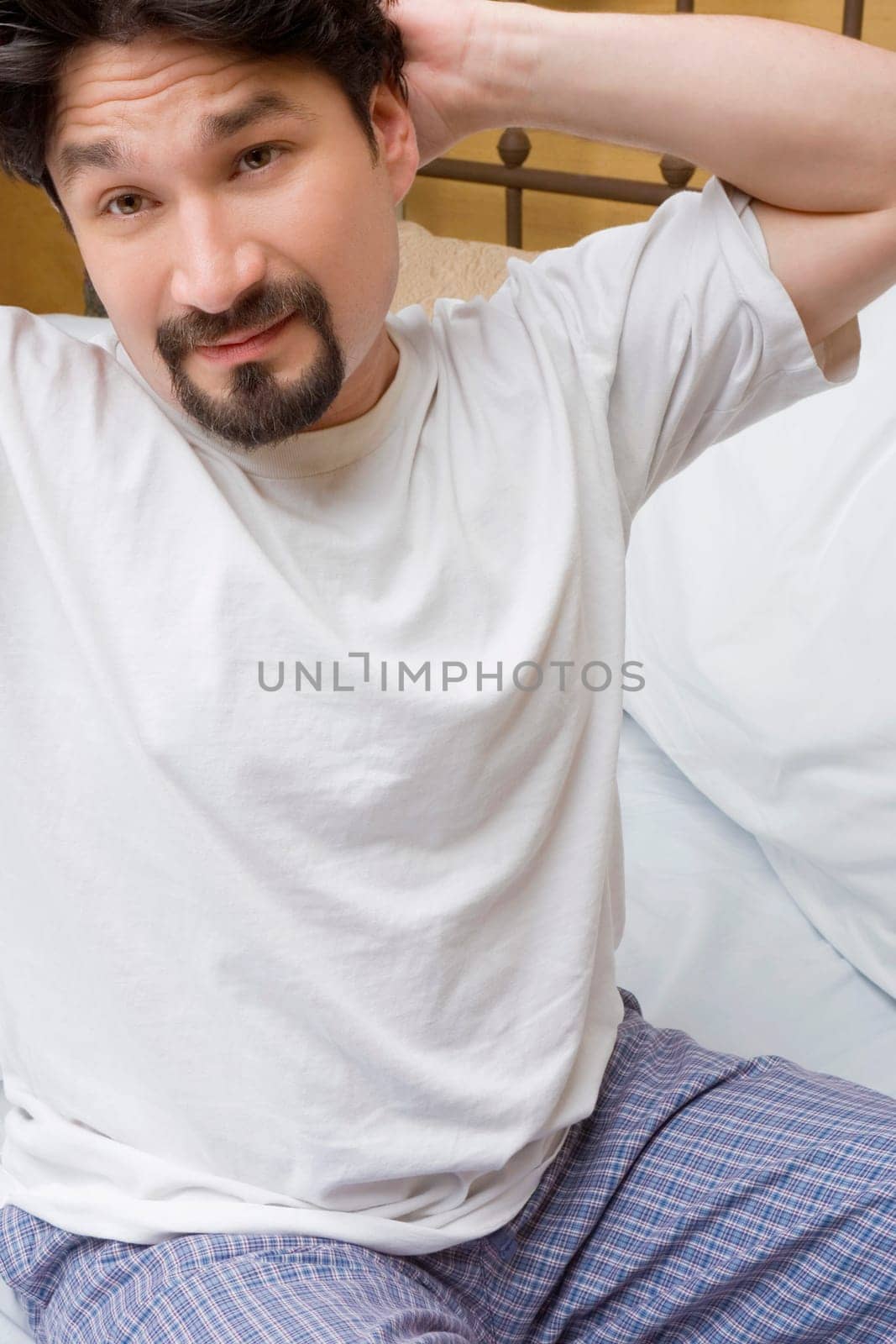 Mid adult man sitting on the bed with his hands behind his back