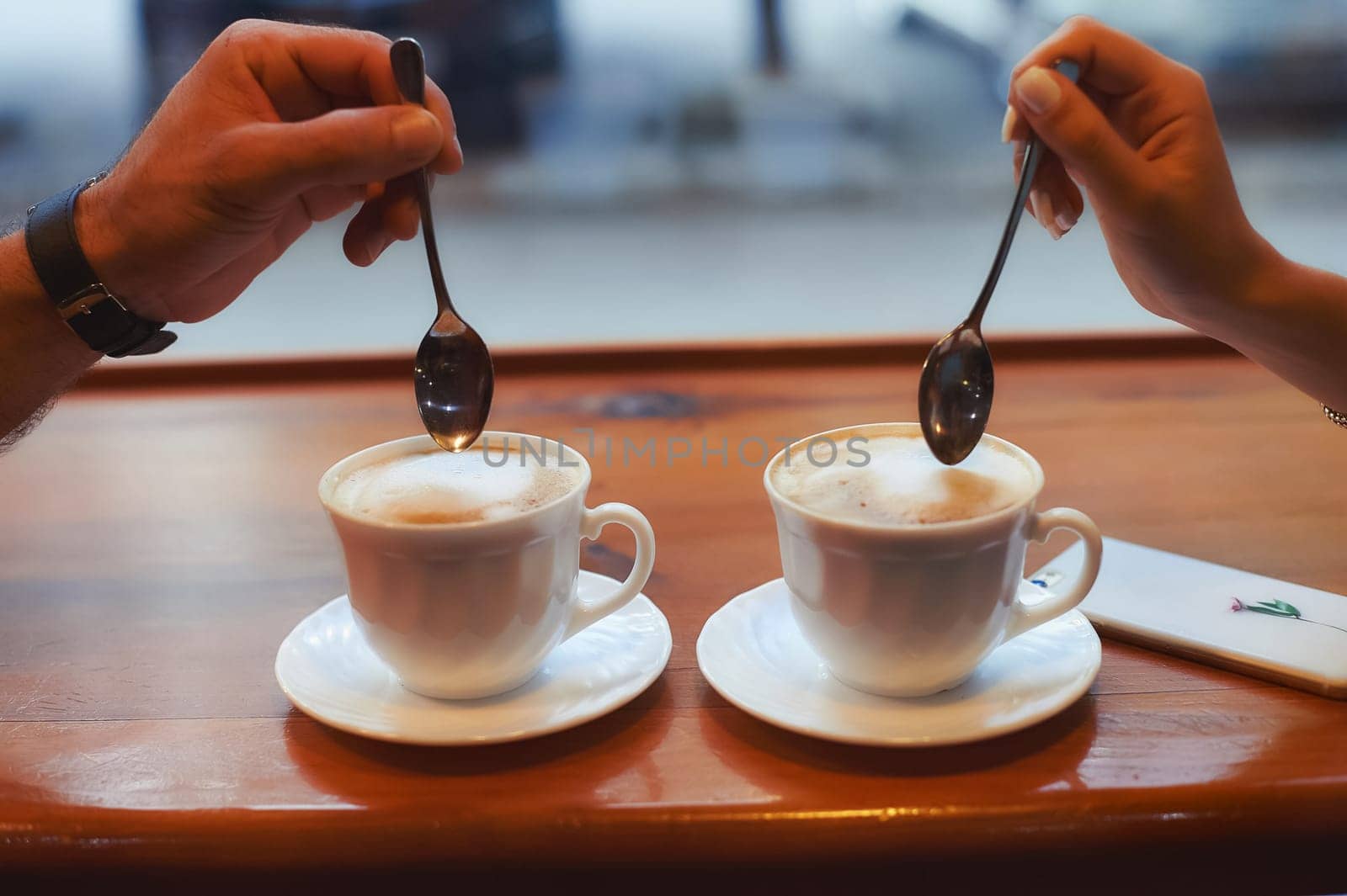 Two cups of coffee on the table, a man's hand and a woman's hand with spoons.