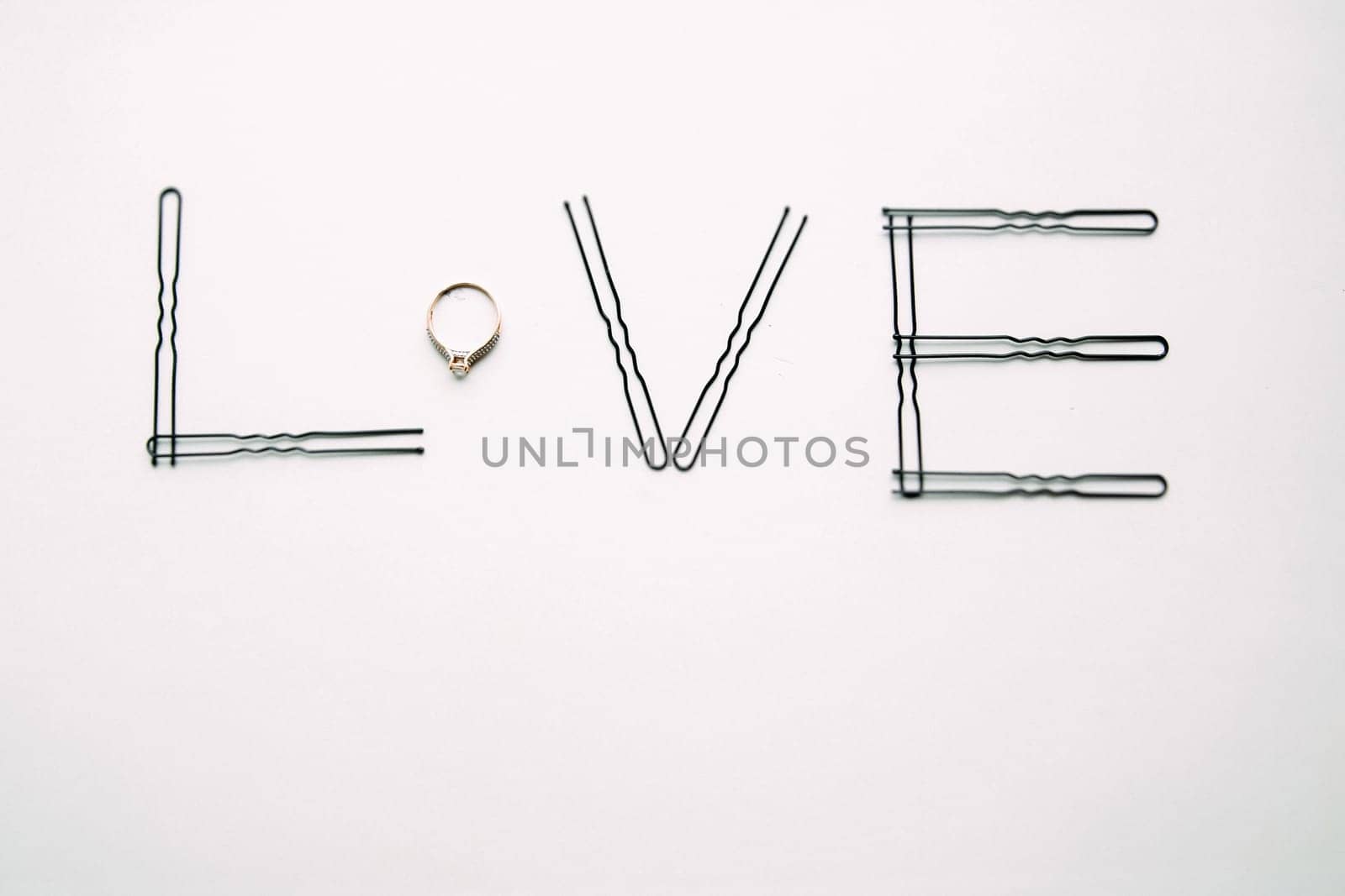 The word love is made of hairpins and an engagement ring.
