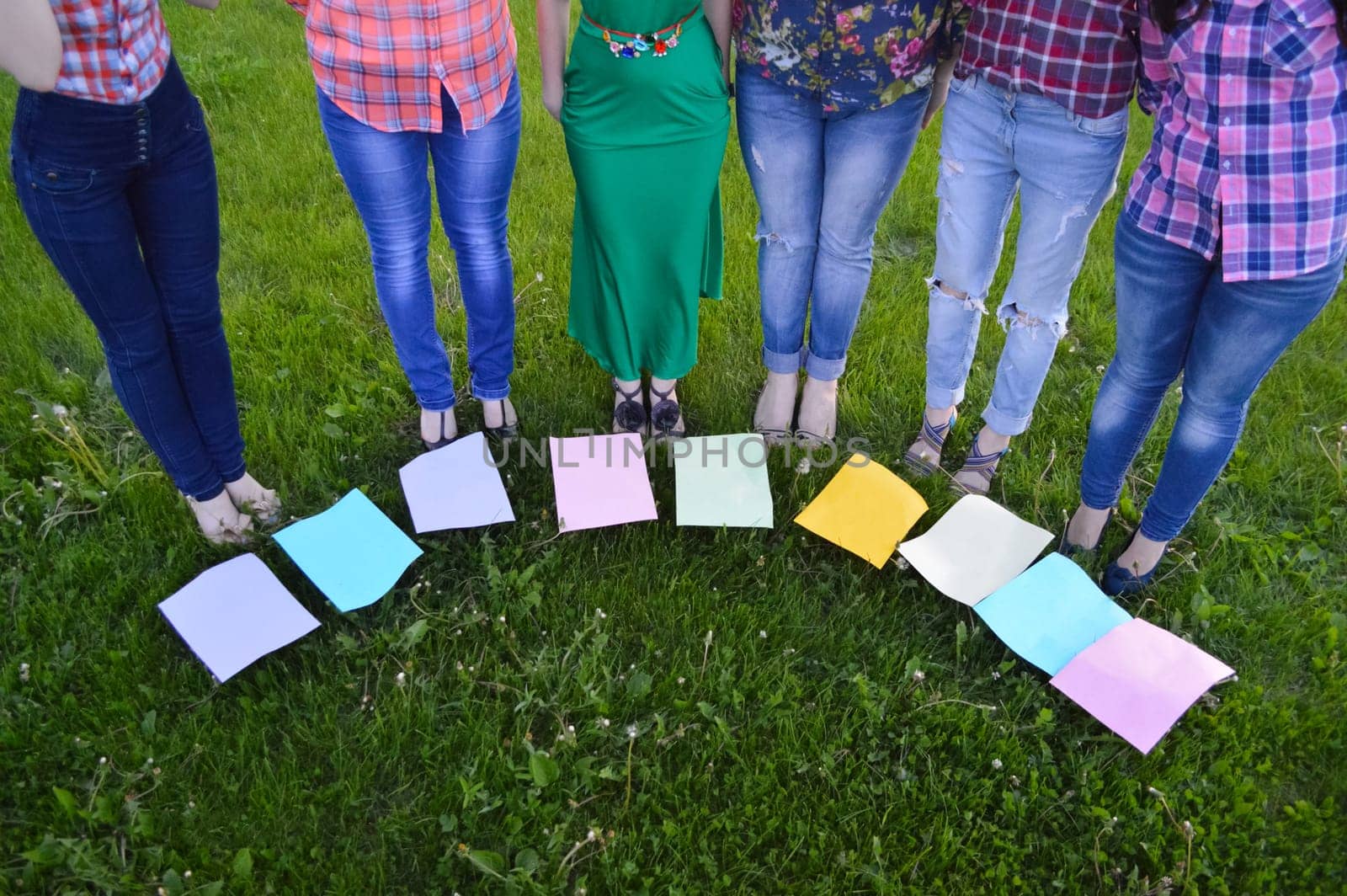 Women stand on the lawn in a semicircle. There are pieces of paper on the grass.