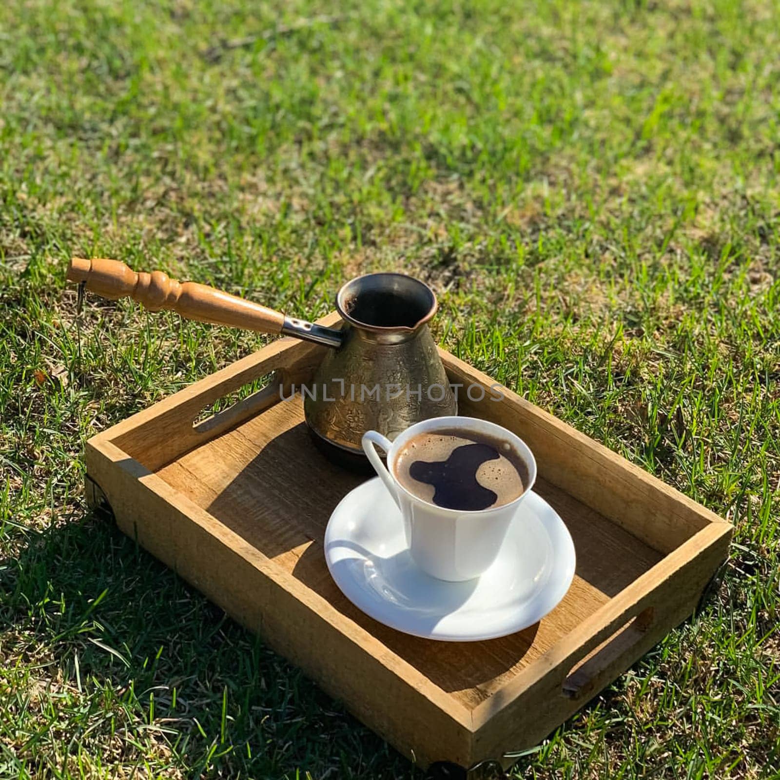 A coffee maker with a handle and a cup of coffee on a wooden tray.