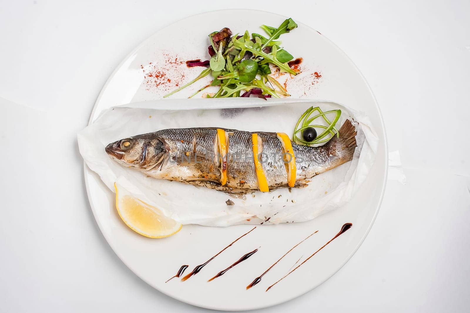 Fried fish with lemon on a white plate. Dandelion salad.