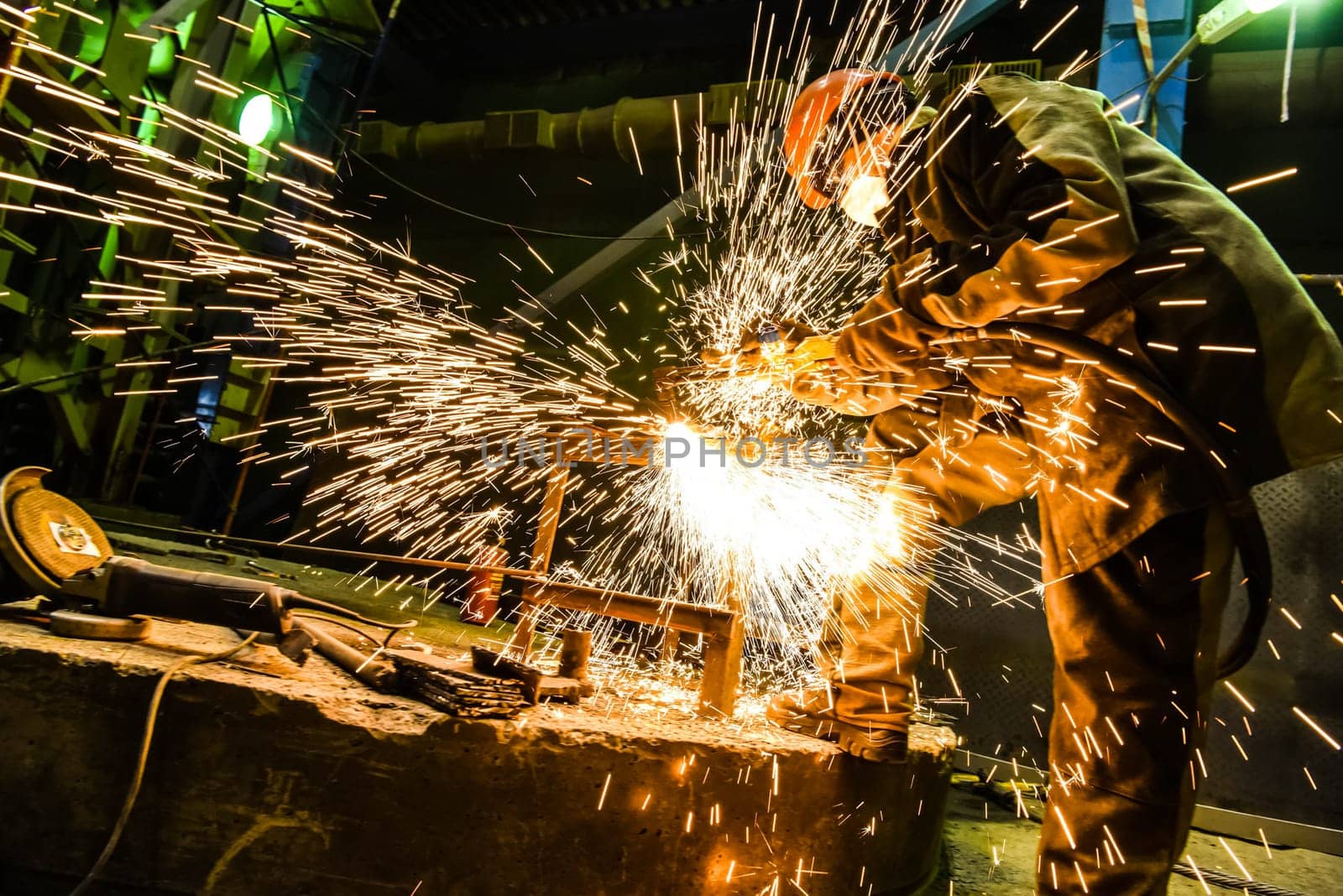 The welder cooks a steel structure. Sparks are flying. The work of a welder.