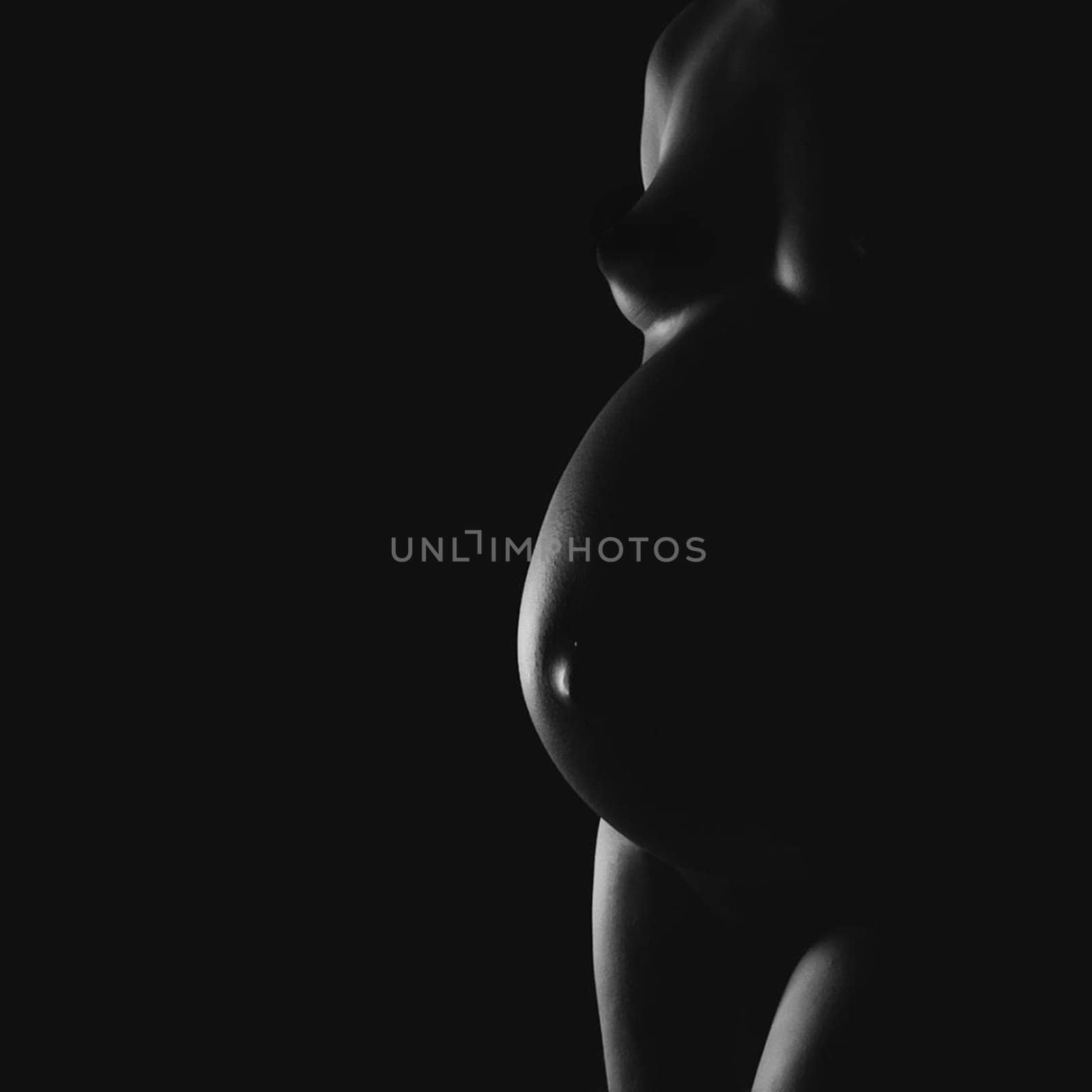 Nude pregnant woman in shadow and side lighting.