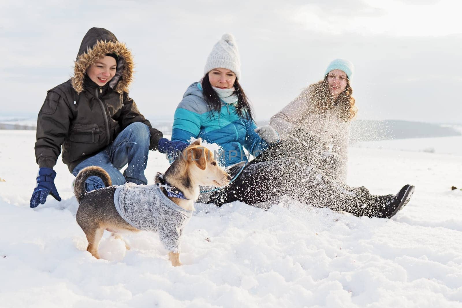family walks the small dog in woolen clothes in the snow during winter time