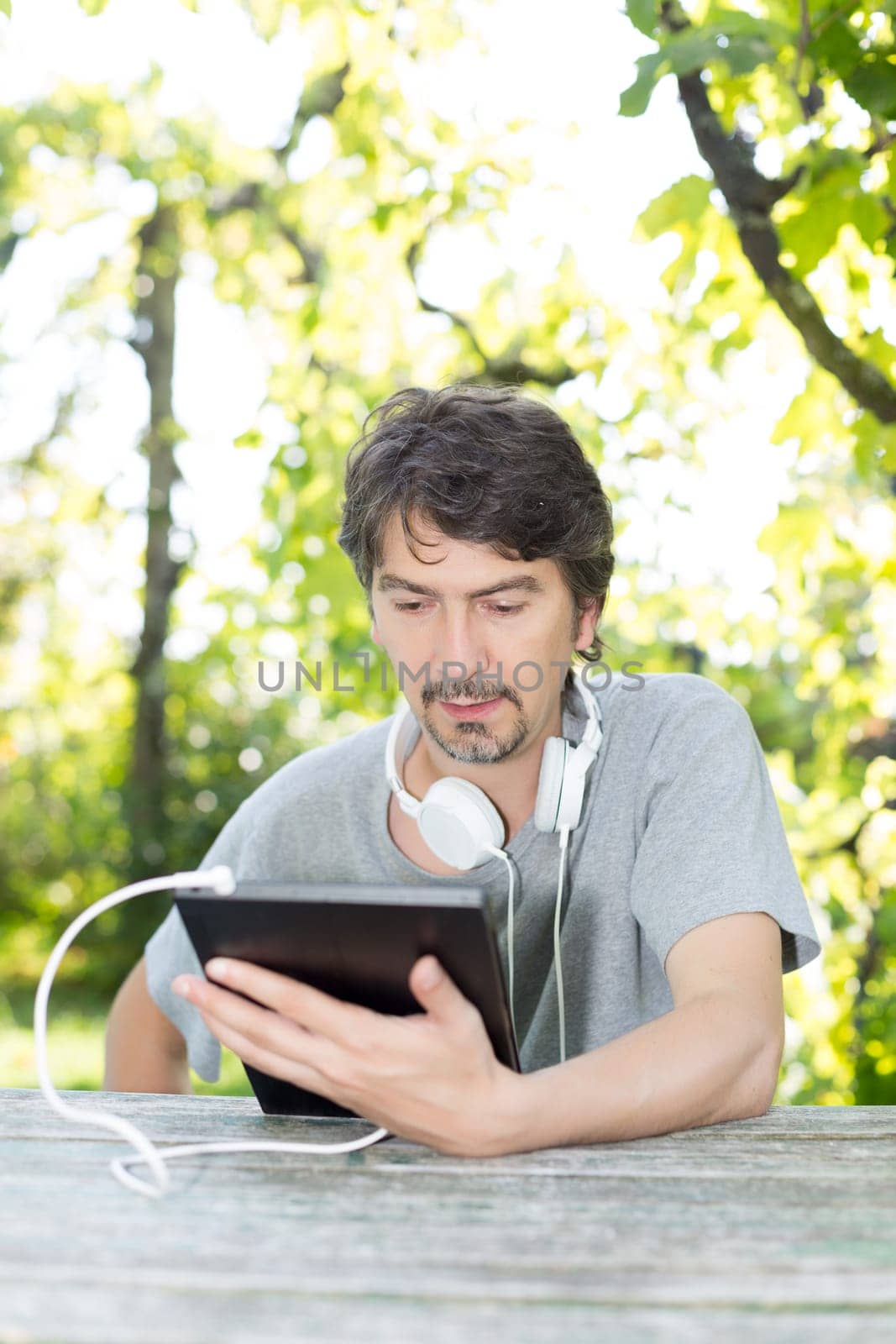 Young man relaxing with a touchscreen computer at a garden