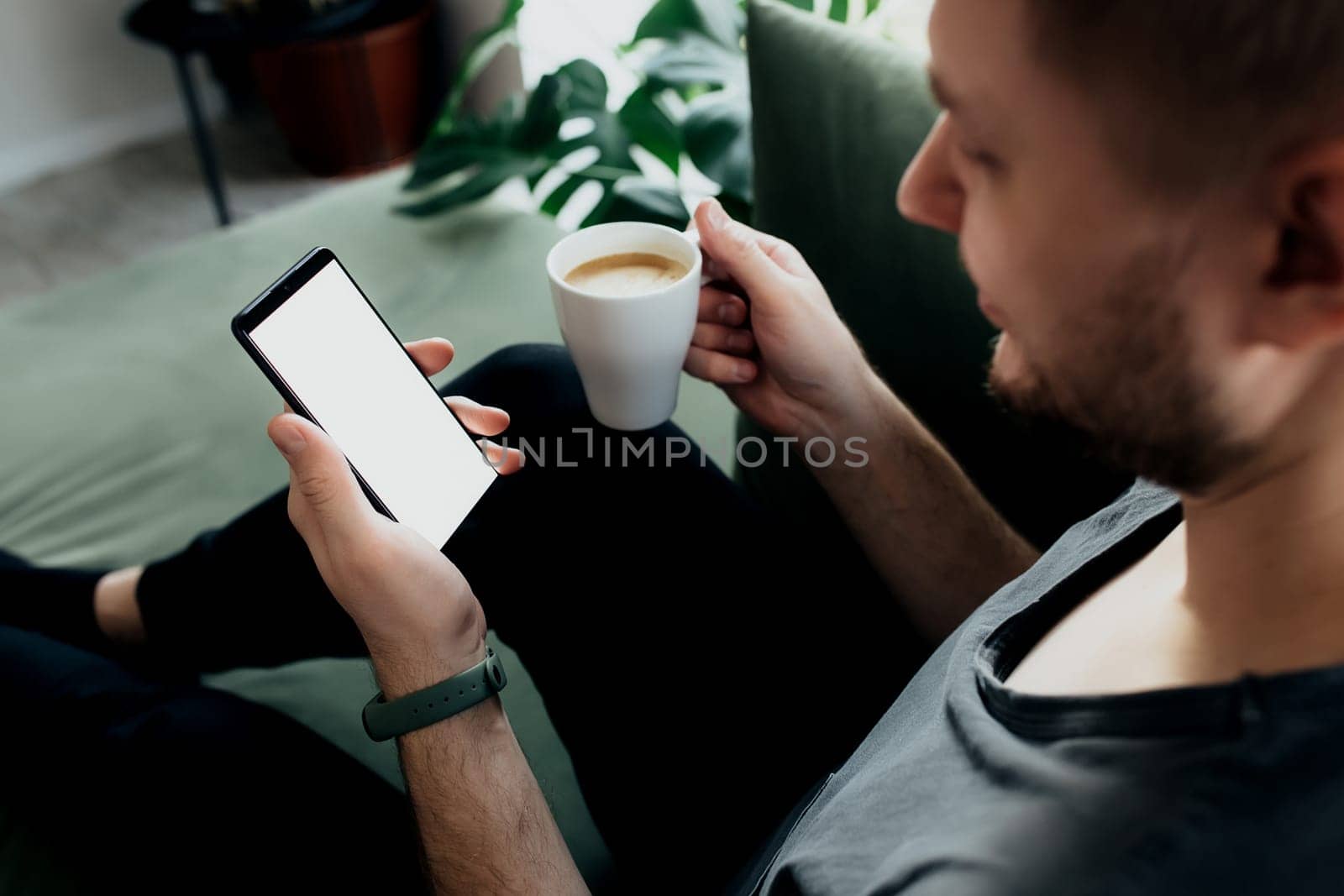 Man holds smartphone with white screen and coffee cup. Blurred background. High quality photo