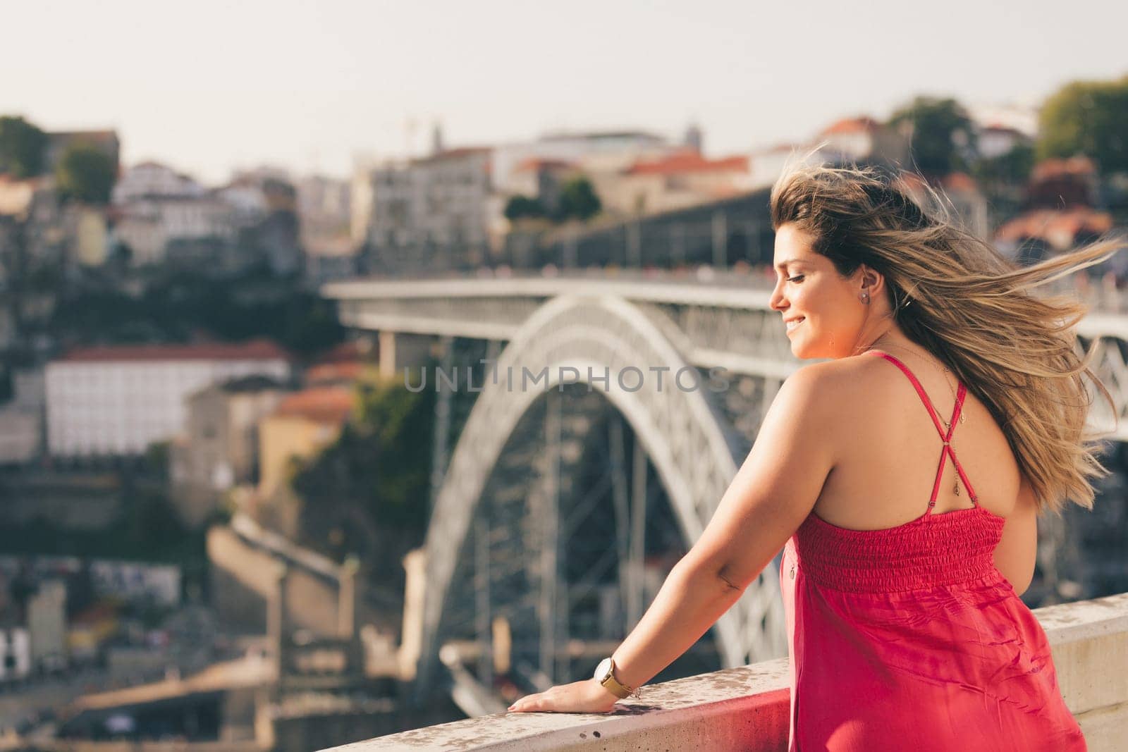 Young woman tourist enjoying beautiful landscape view on the old town with river and famous iron bridge during the sunset in Porto city, Portugal