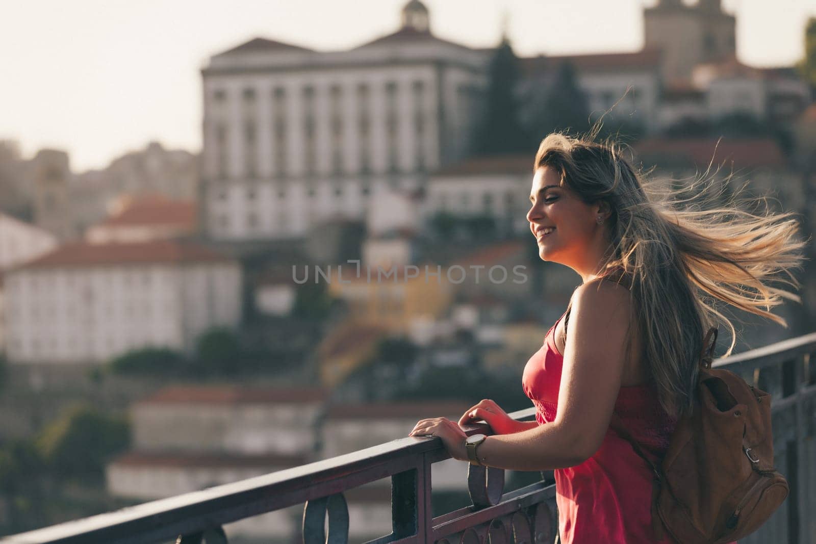 Young woman tourist enjoying beautiful landscape view on the old town with river and famous iron bridge during the sunset in Porto city, Portugal