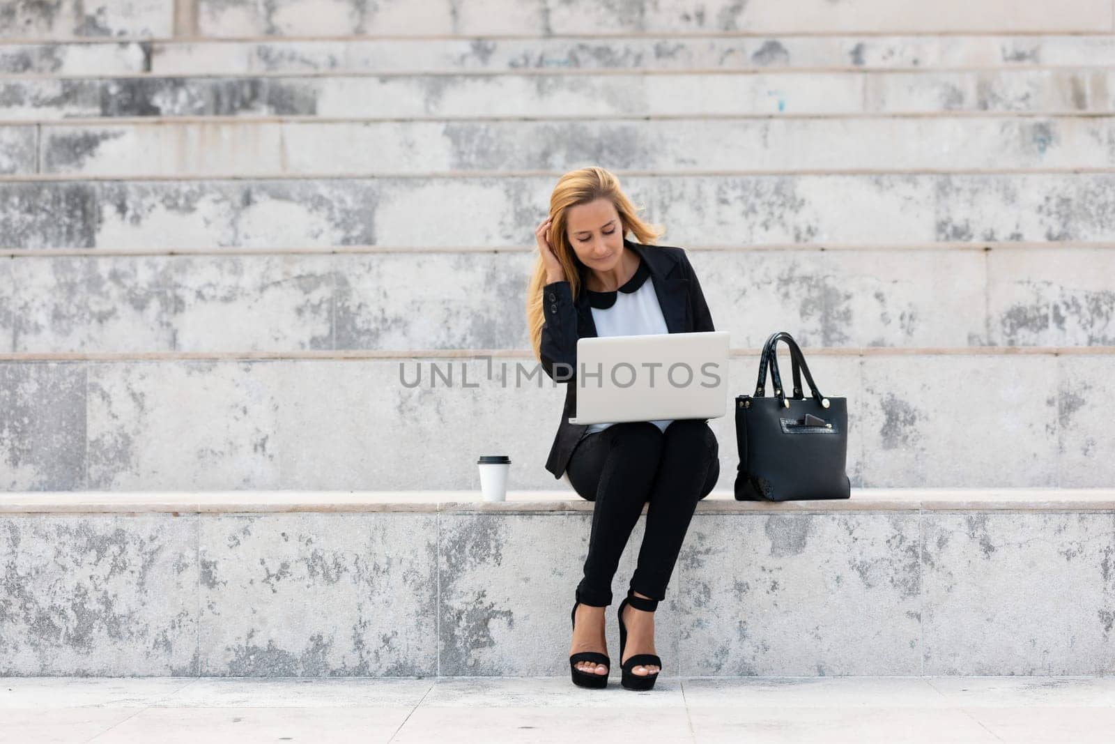 Young attractive businesswoman sitting on the stairs and using modern laptop
