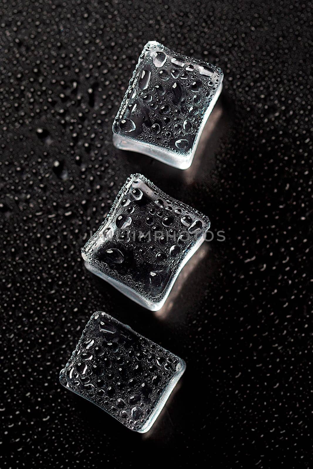 Three Ice cubes on black color texture. Concept art. Minimal surrealism. Flat lay with copy space. Soft focus. Vertical orientation.