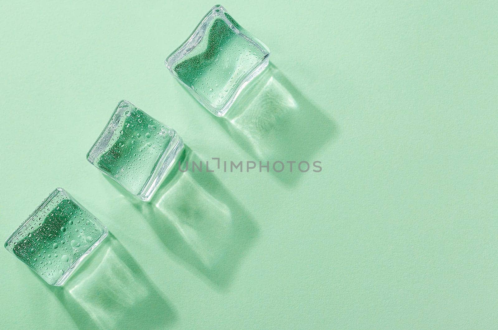 Three Ice cubes with reflexes on pastel green color background. Concept art. Minimal surrealism. Flat lay with copy space. Soft focus.
