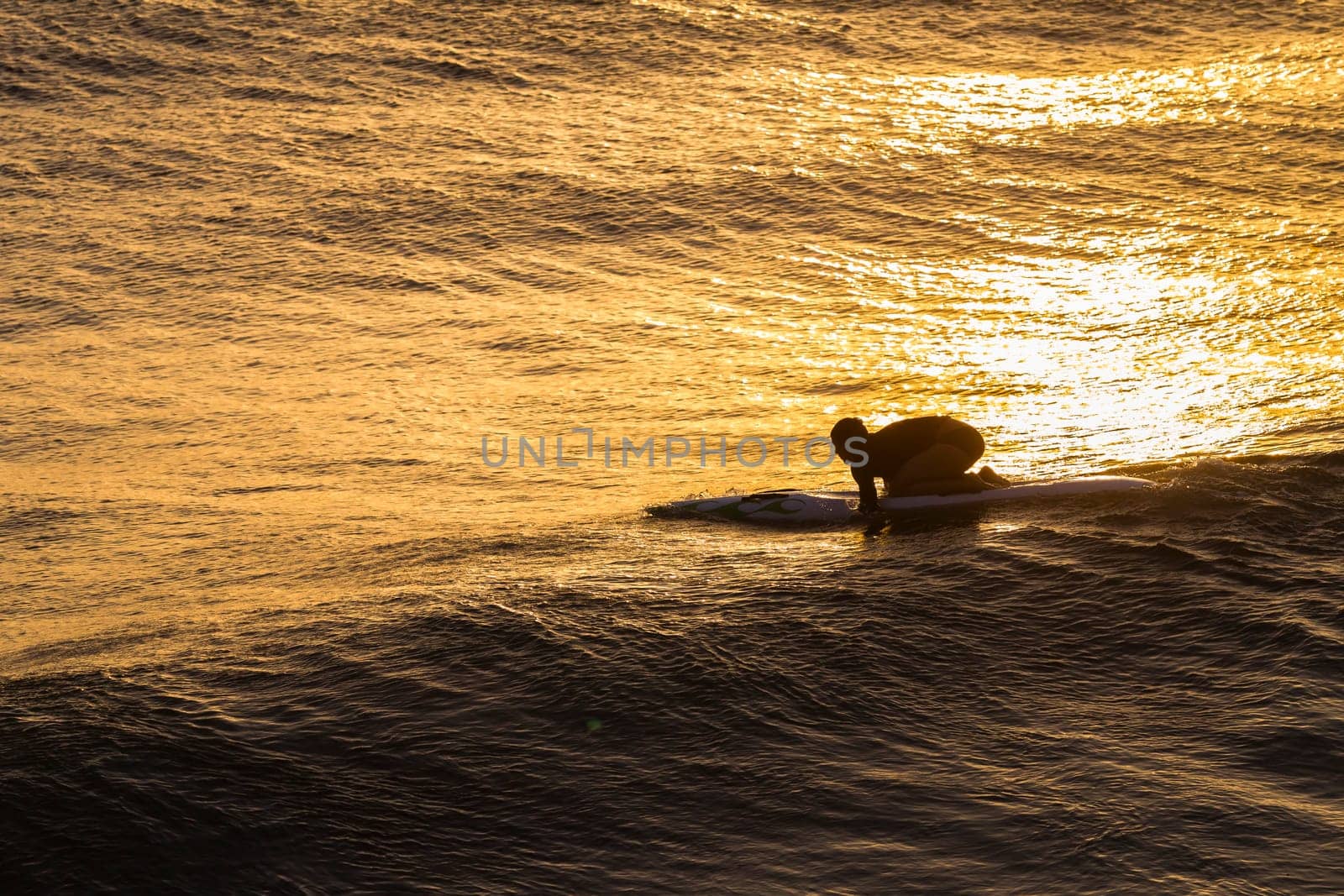 Lifeguard  athlete trains dawn sunrise on rescue craft paddling out through ocean wave swells.