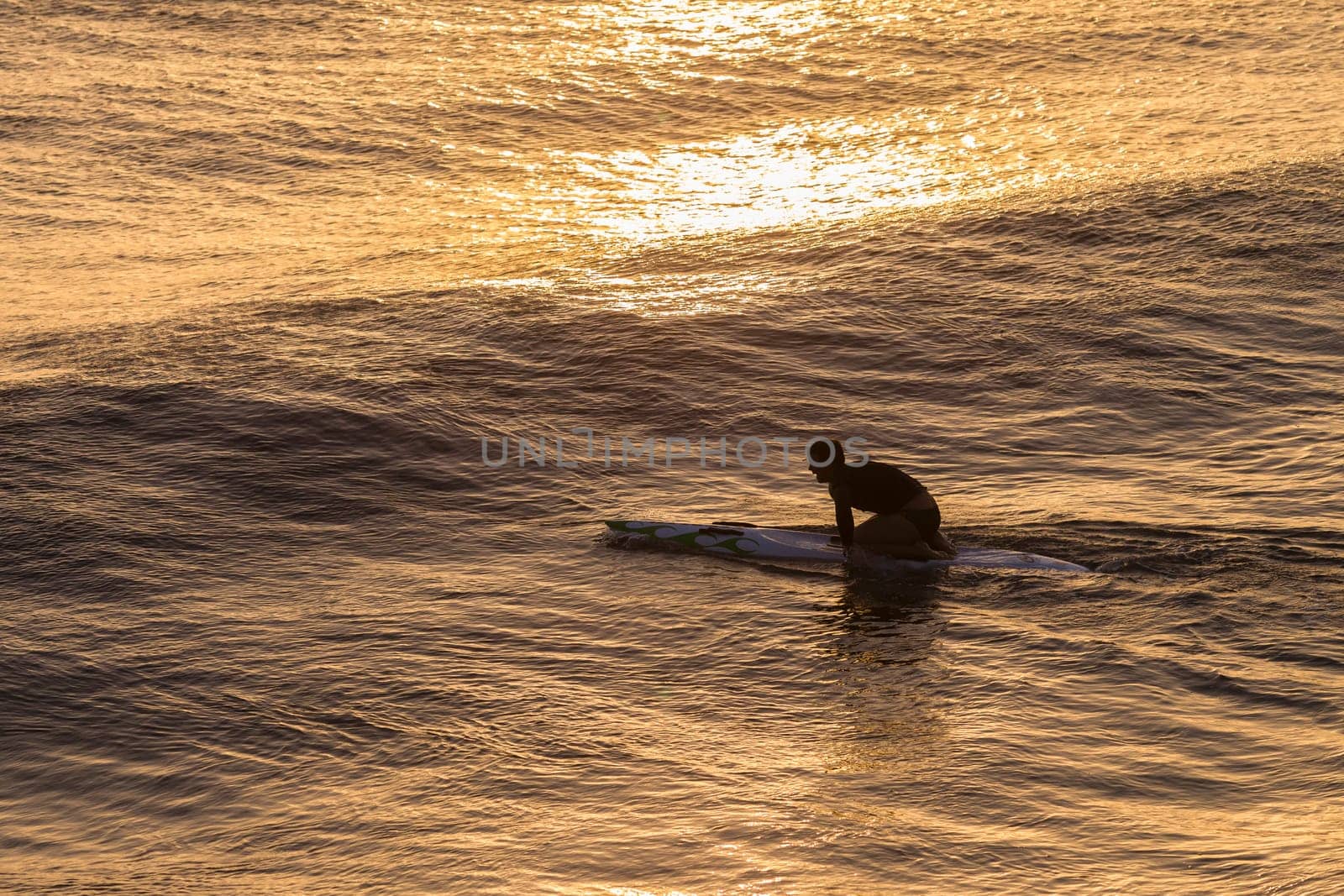 Lifeguard  athlete trains dawn sunrise on rescue craft paddling out through ocean wave swells.