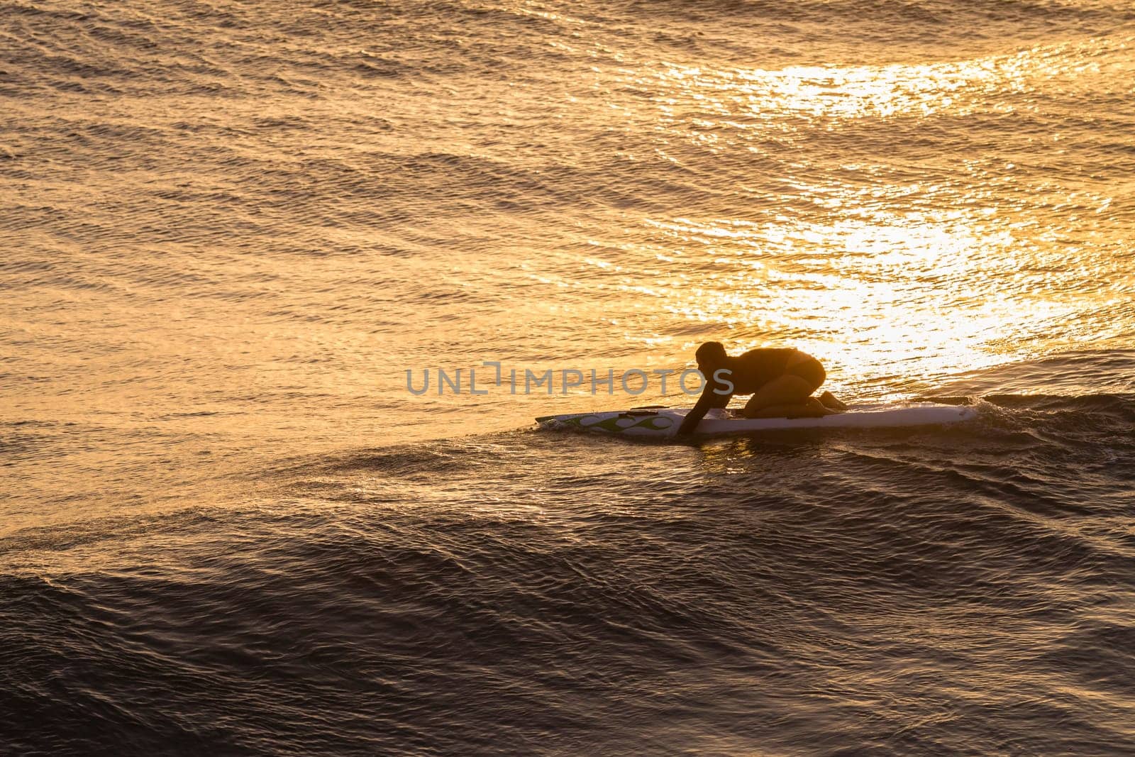 Lifeguard  athlete trains dawn sunrise on rescue craft paddling out through ocean wave swells.