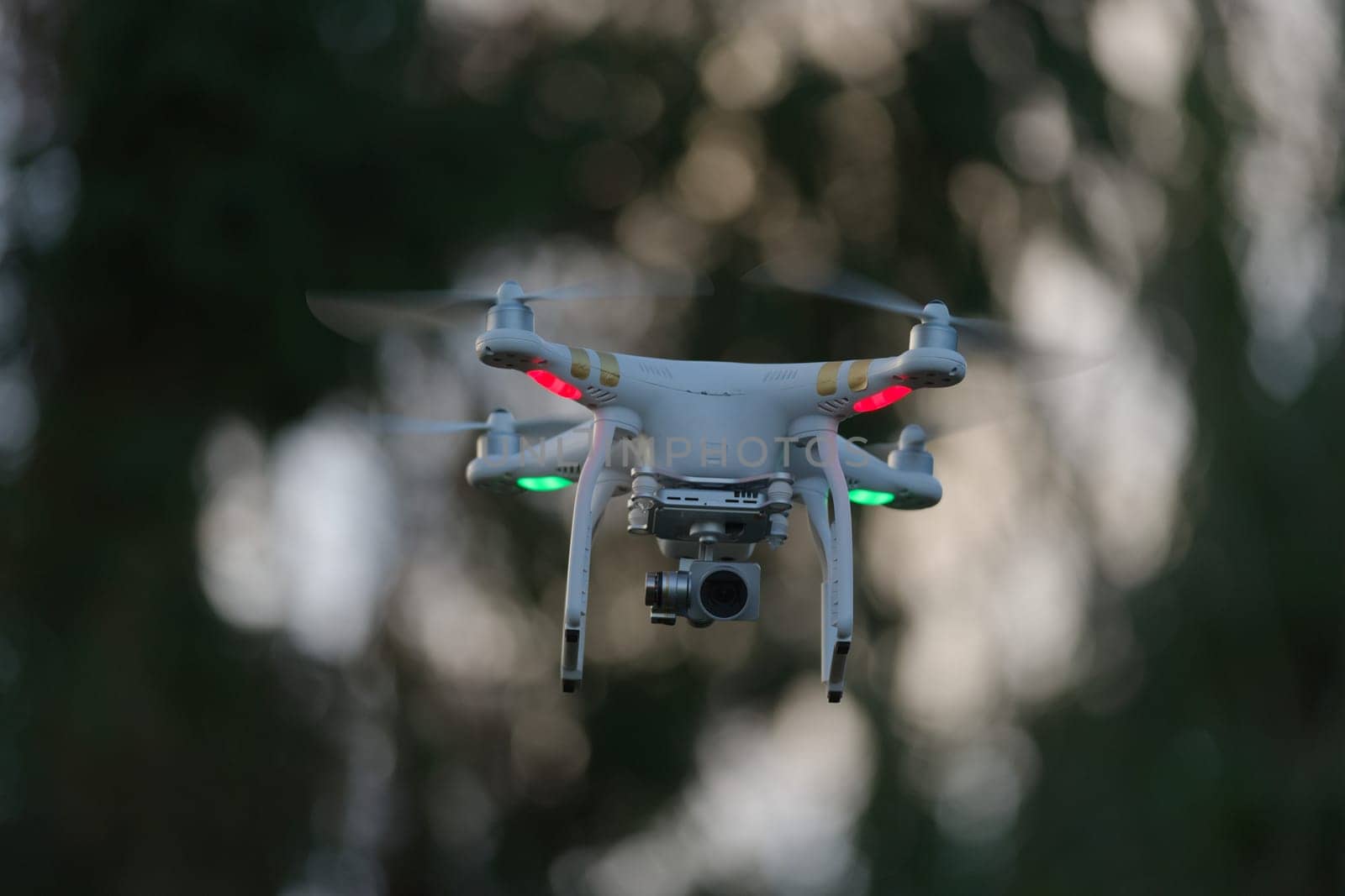 1 - Drone quadcopter hovering in front of trees, blurred background of defocused trees at sunset