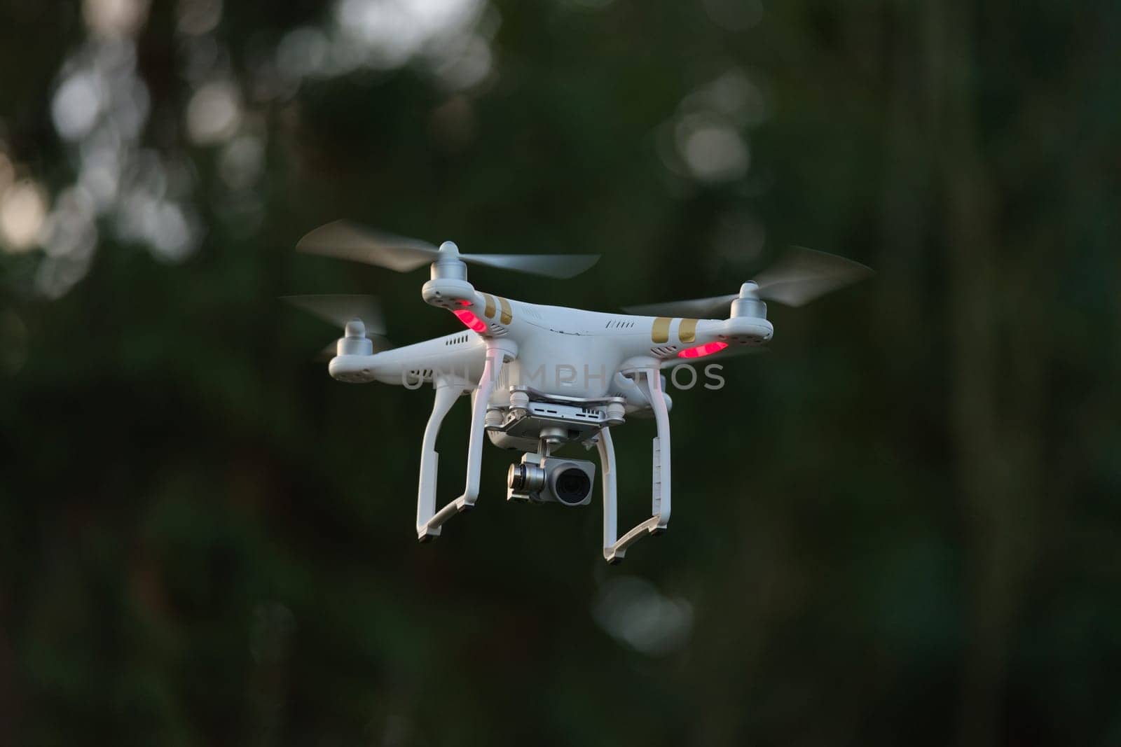 6 - Common white camera drone used for surveillance, plain background. Logos all removed, propellers blurred from moving at high speed