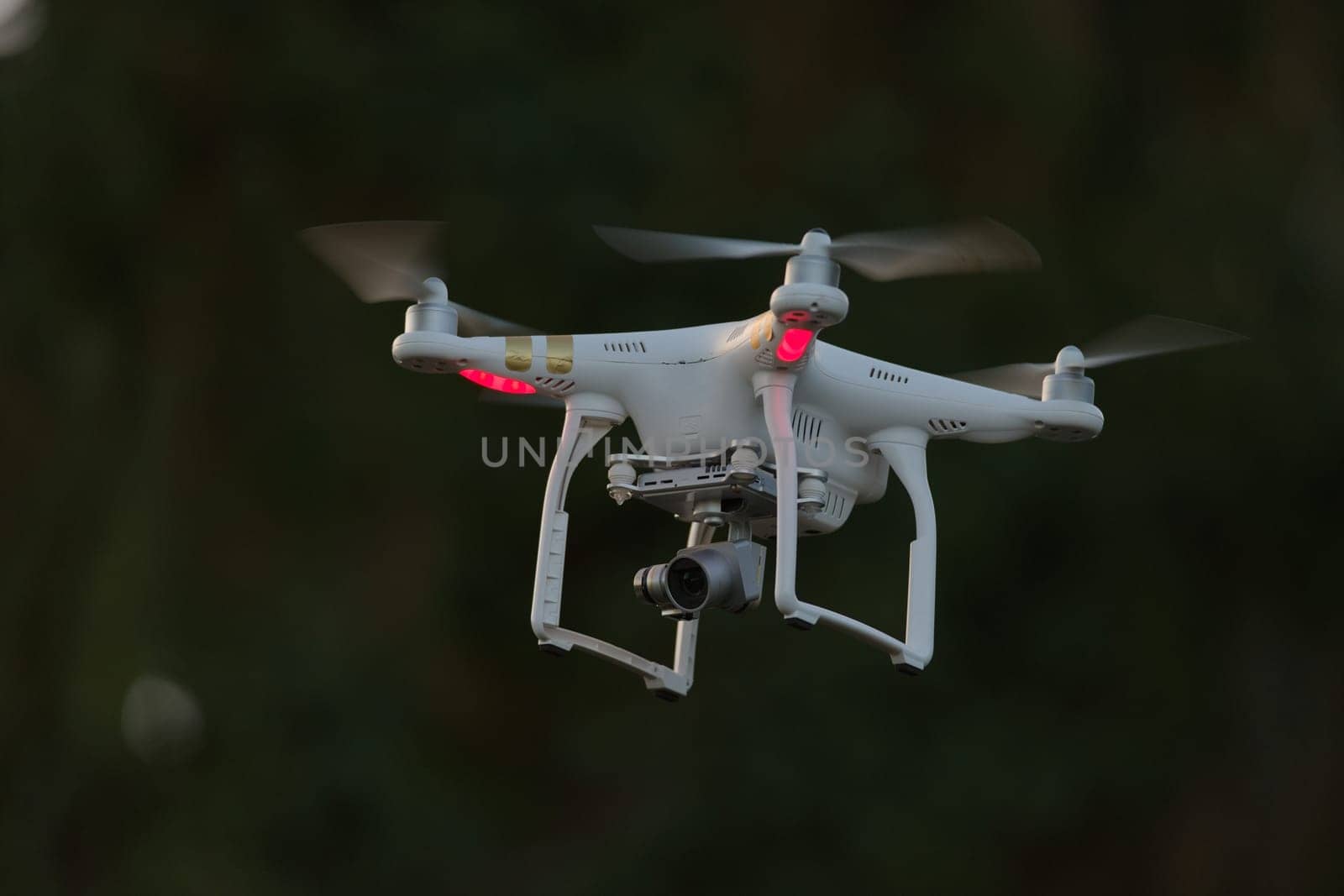 20 - Isolated quadcopter camera drone carrying digital camera. Plain dark background with selective focus, leaving the bright white drone as subject.