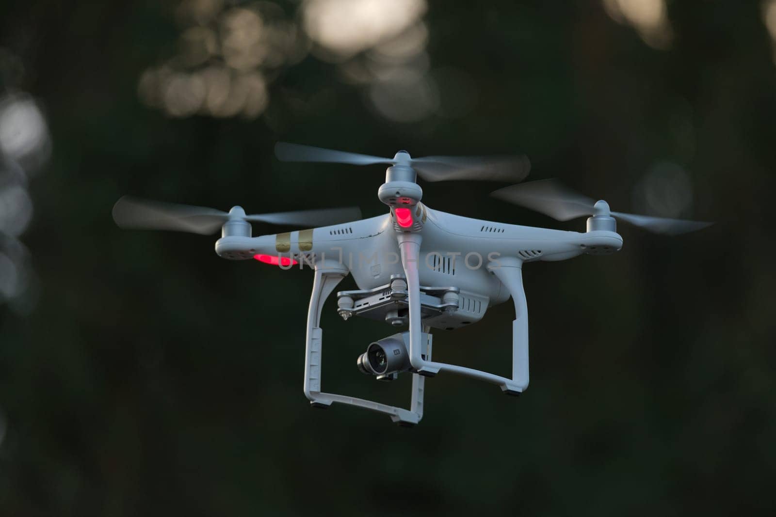 17 - White quad copter drone with red lights on a dark background. Unmanned ariel vehicle with camera gimbal payload used for filming video or photos