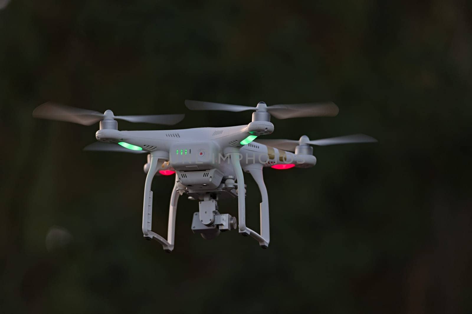 25 - Rear view of professional quadcopter camera drone hovering. Looking from behind shows the battery status indicator lights and green orientation.