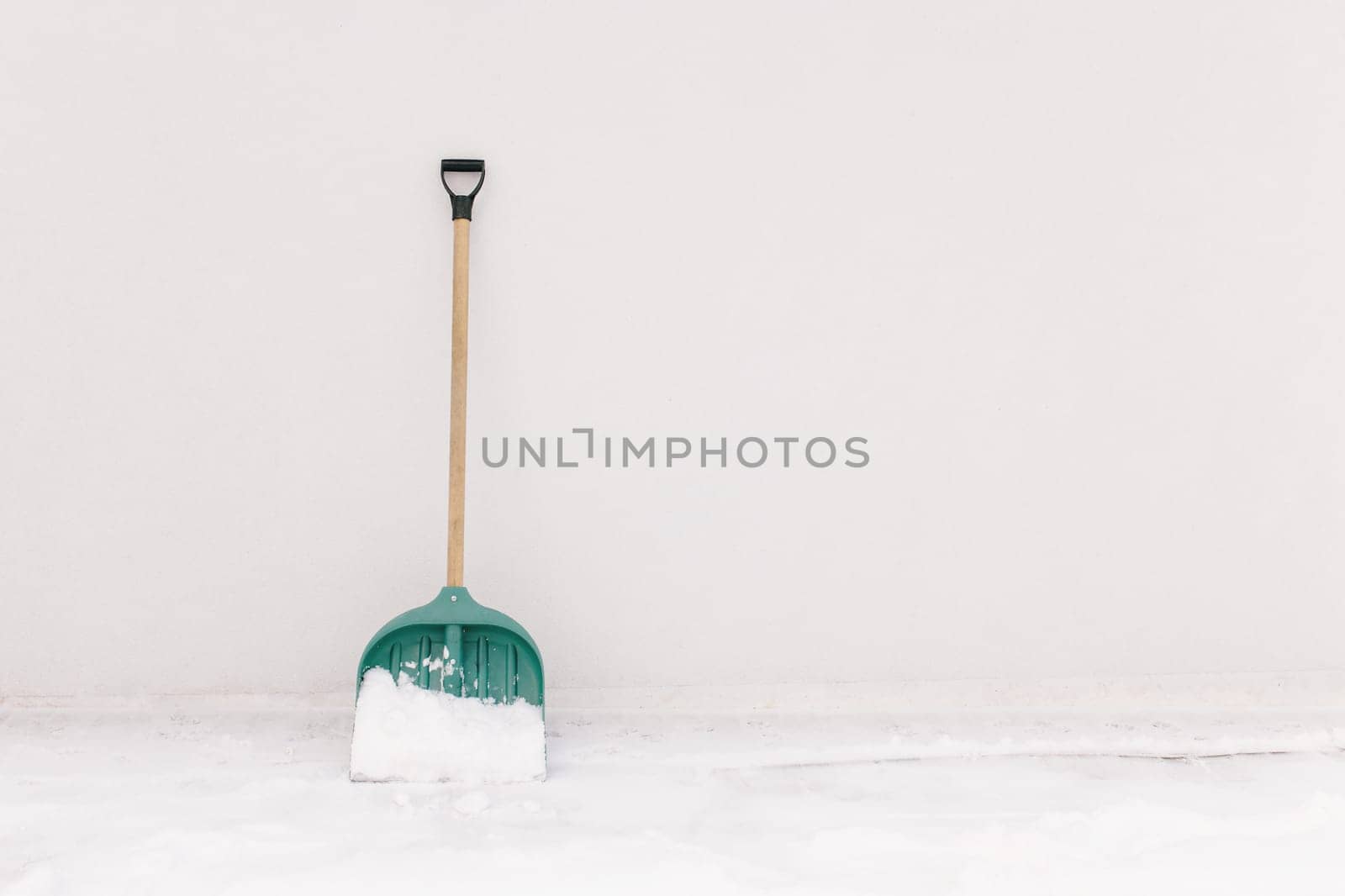 Snow shovel propped against the white wall of the house. High quality photo