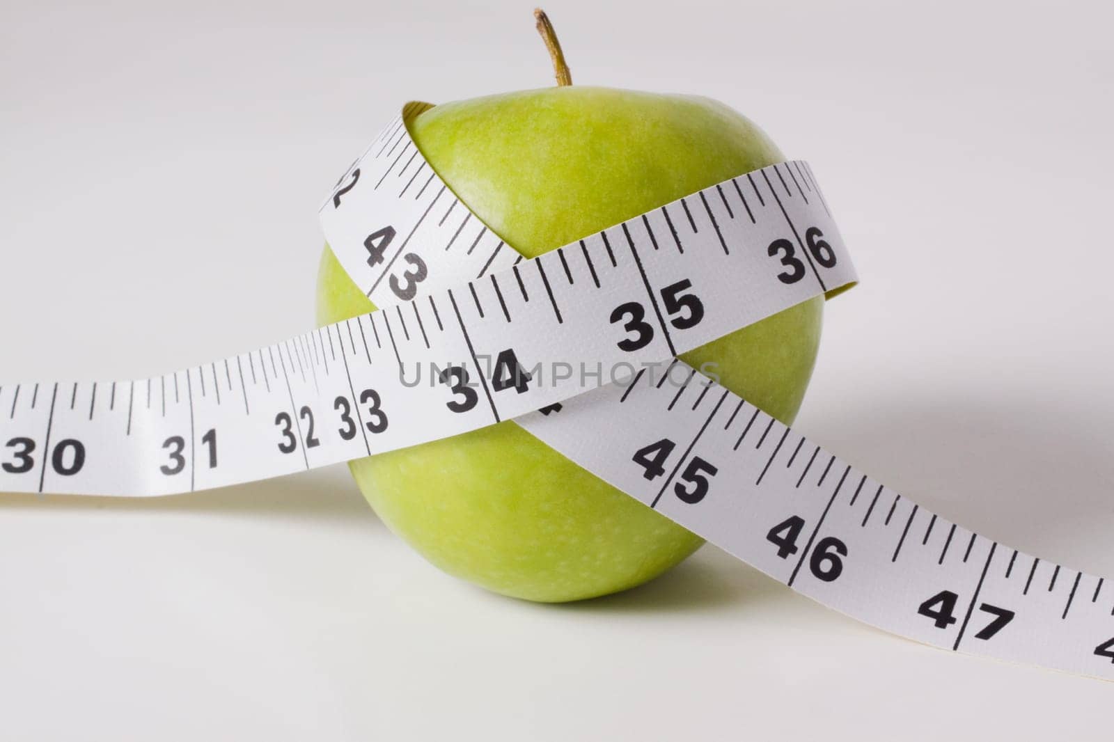 Close_up of a tape measure wrapped around a green apple