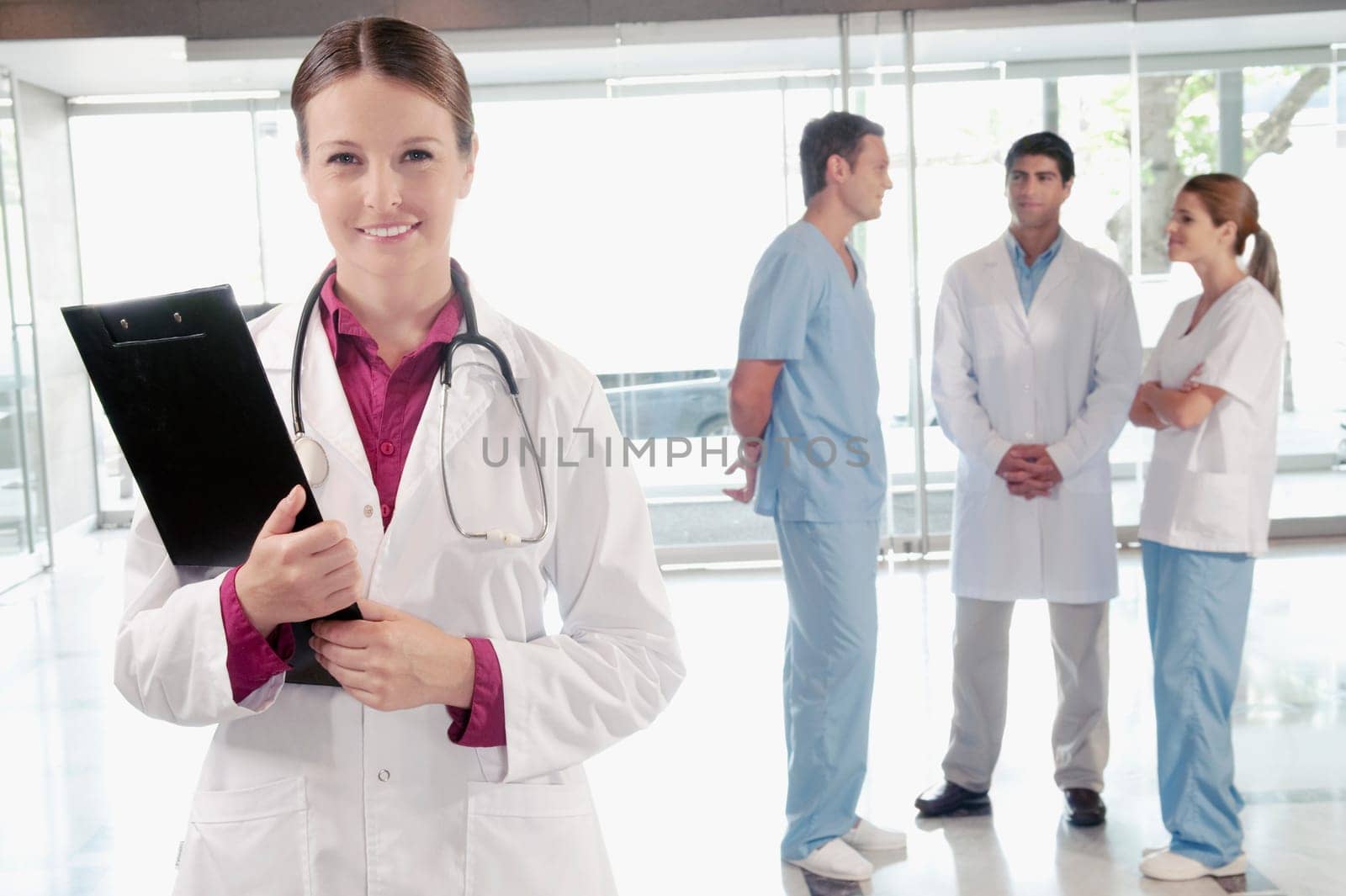 Female doctor holding a clipboard with her colleagues discussing in the background