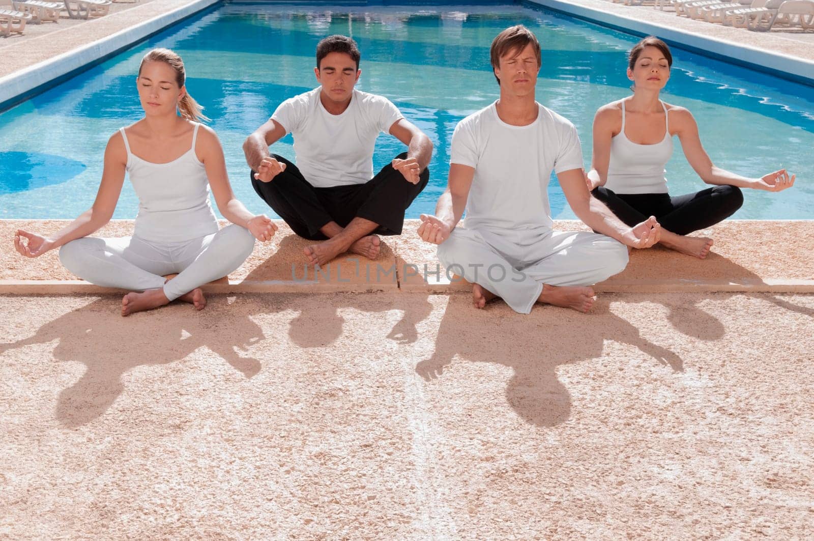 Four friends practicing yoga at the poolside