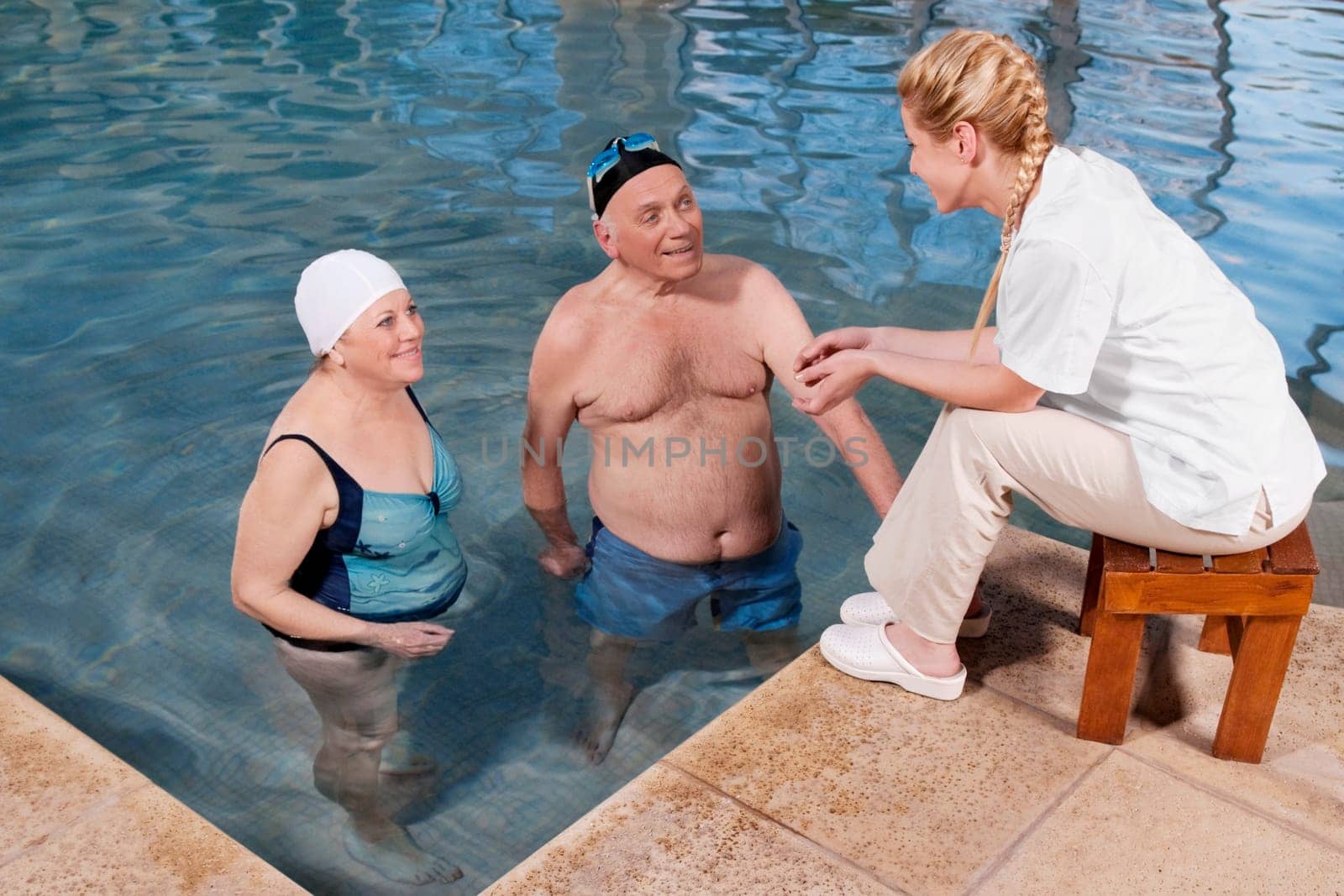 Couple enjoying in a swimming pool with a health worker at poolside