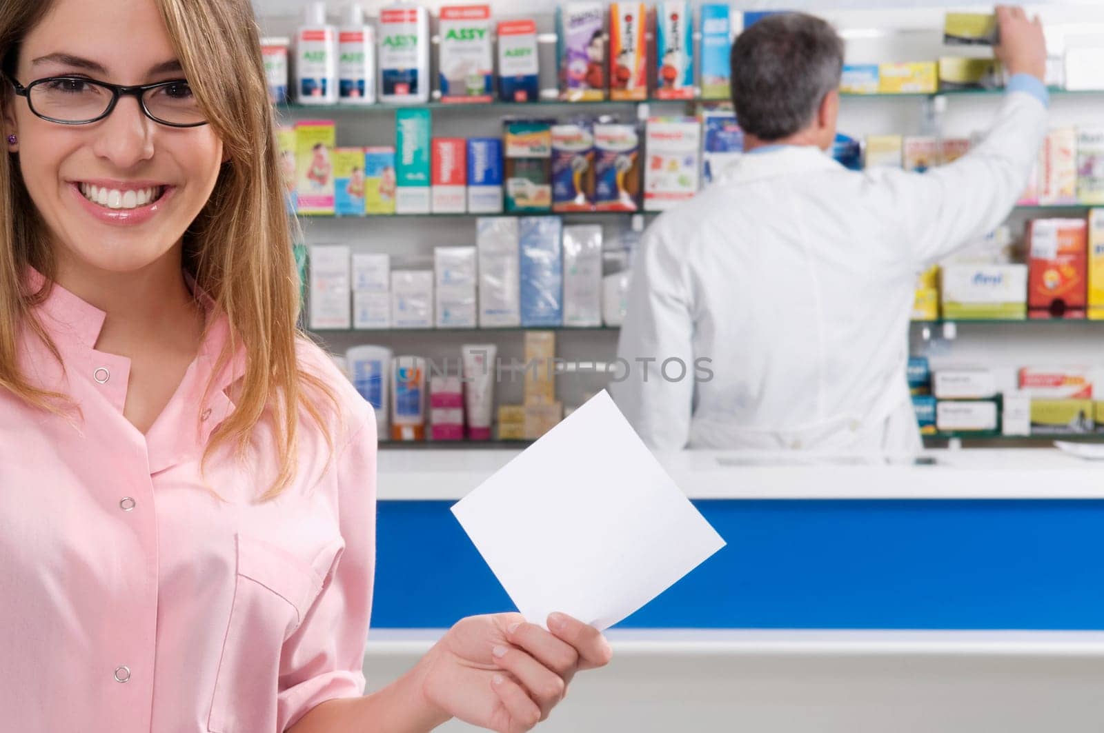 Female pharmacist holding a prescription and a male pharmacist in the background