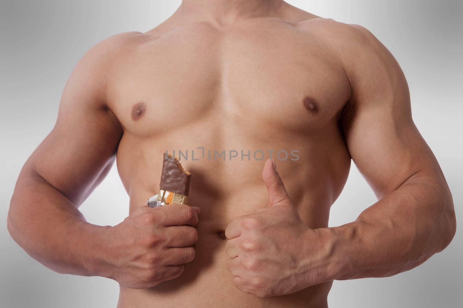 Mid section view of a man holding a protein bar and showing thumbs up sign