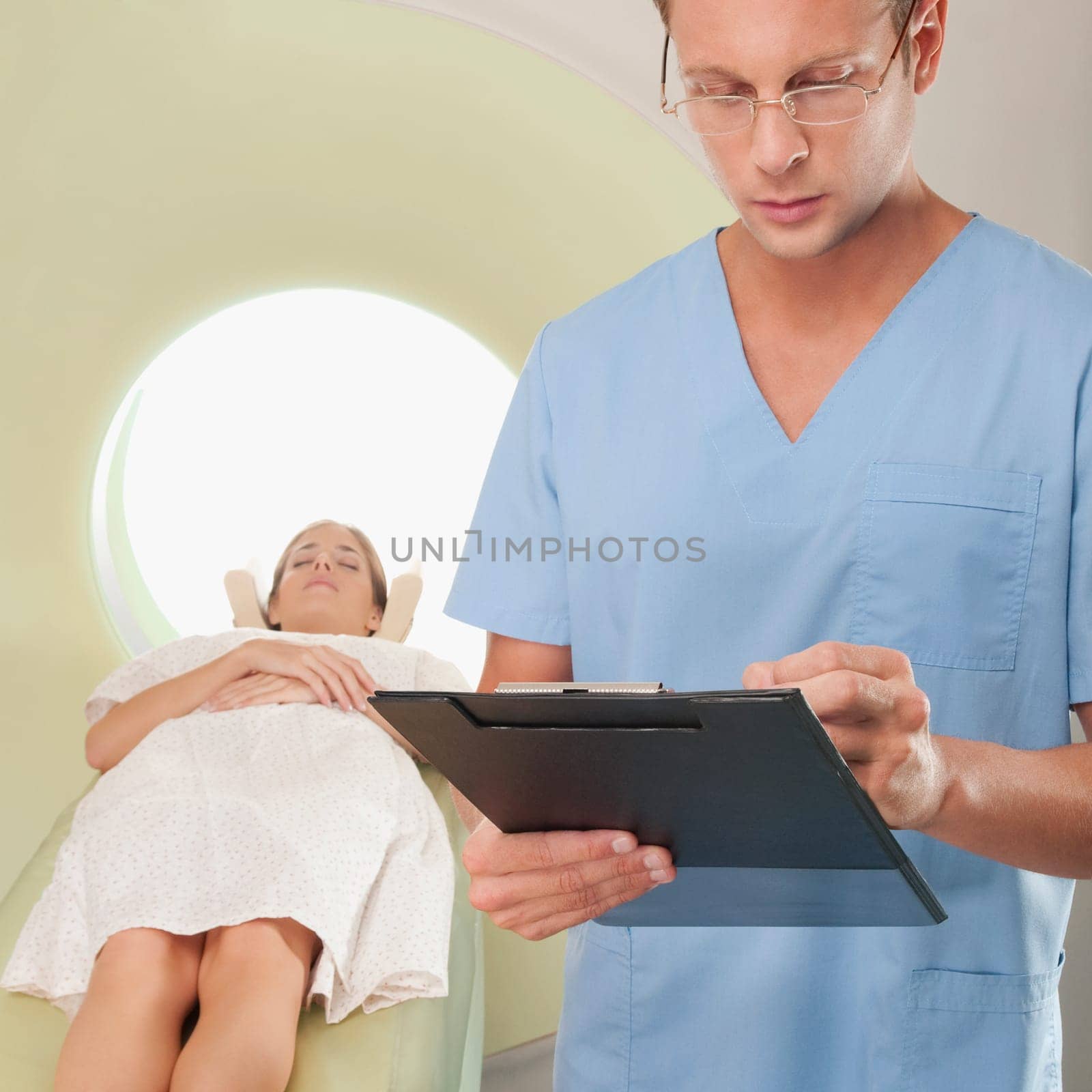 Surgeon checking medical report with a patient undergoing an MRI scan in background